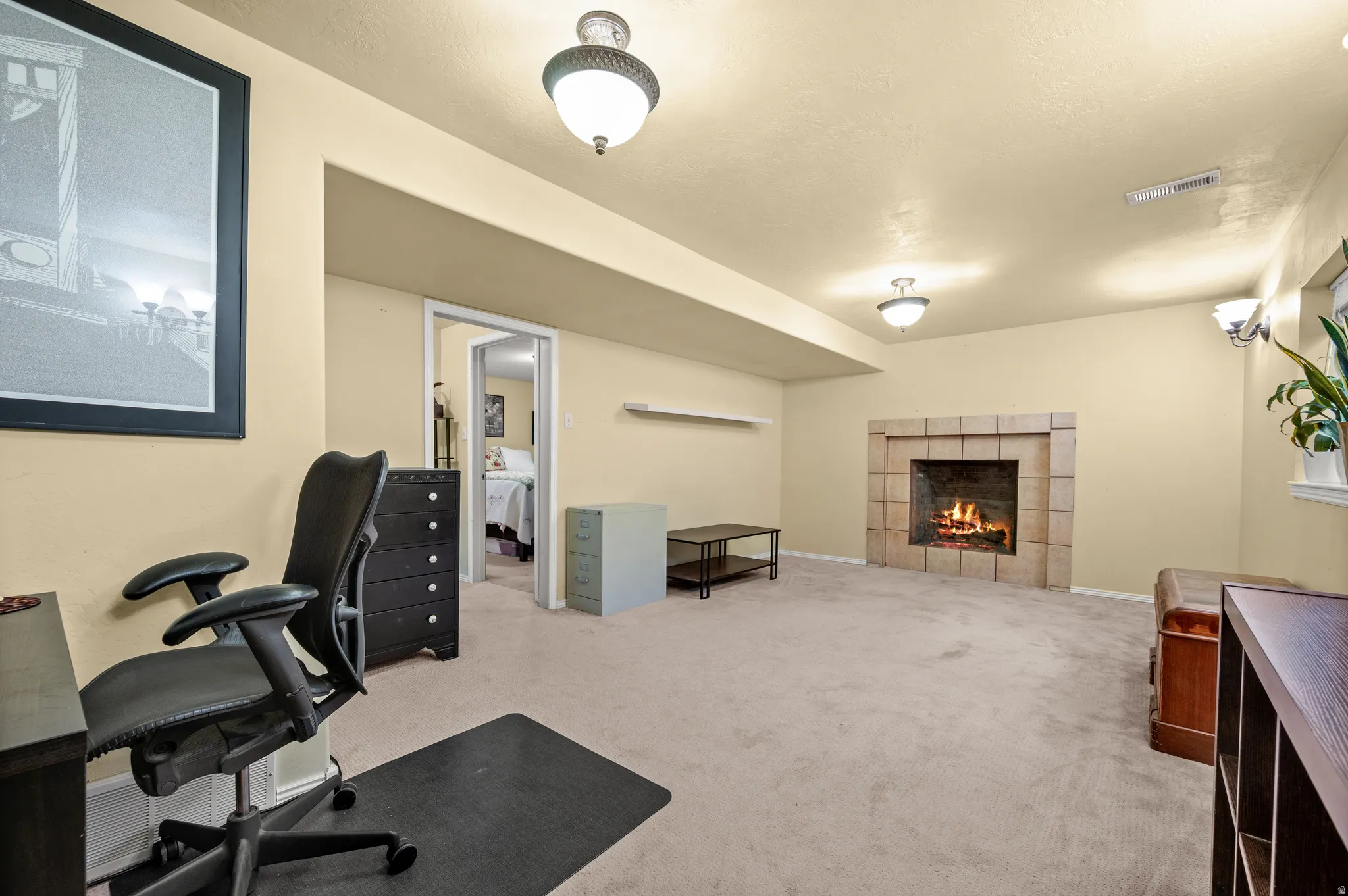 Carpeted room featuring a tiled fireplace with hearth, recessed lighting, and a doorway opening to an additional room