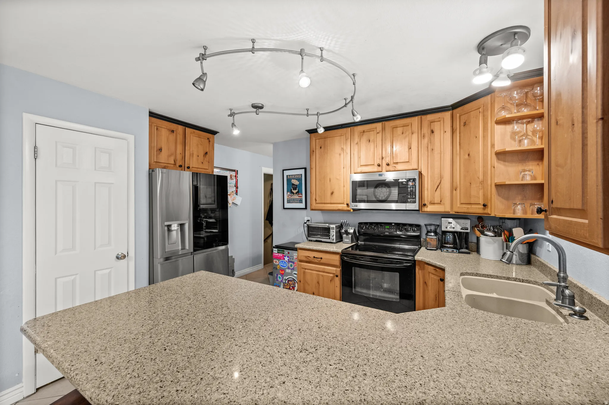 Kitchen featuring light wood cabinetry with dark trim, light speckled countertops, and stainless steel appliances
