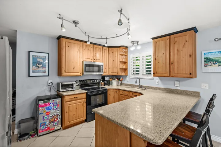 U-shaped kitchen featuring wood cabinetry with dark trim, light-toned countertops, tile flooring, and integrated stainless steel microwave
