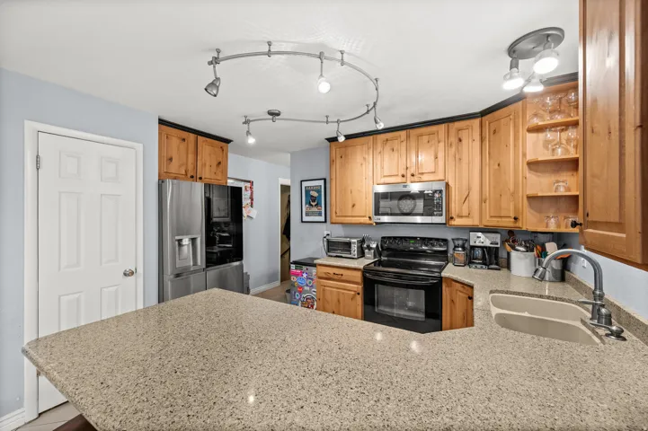 Kitchen featuring light wood cabinetry with dark trim, light speckled countertops, and stainless steel appliances