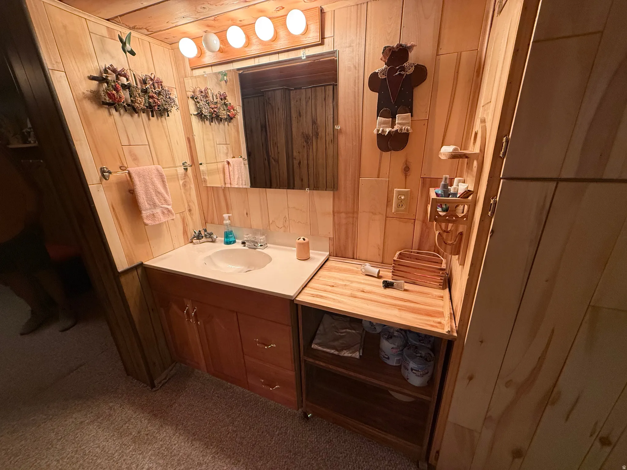 Wood-paneled bathroom featuring a vanity with a light-colored countertop and integrated sink, a wall-mounted mirror, and overhead lighting