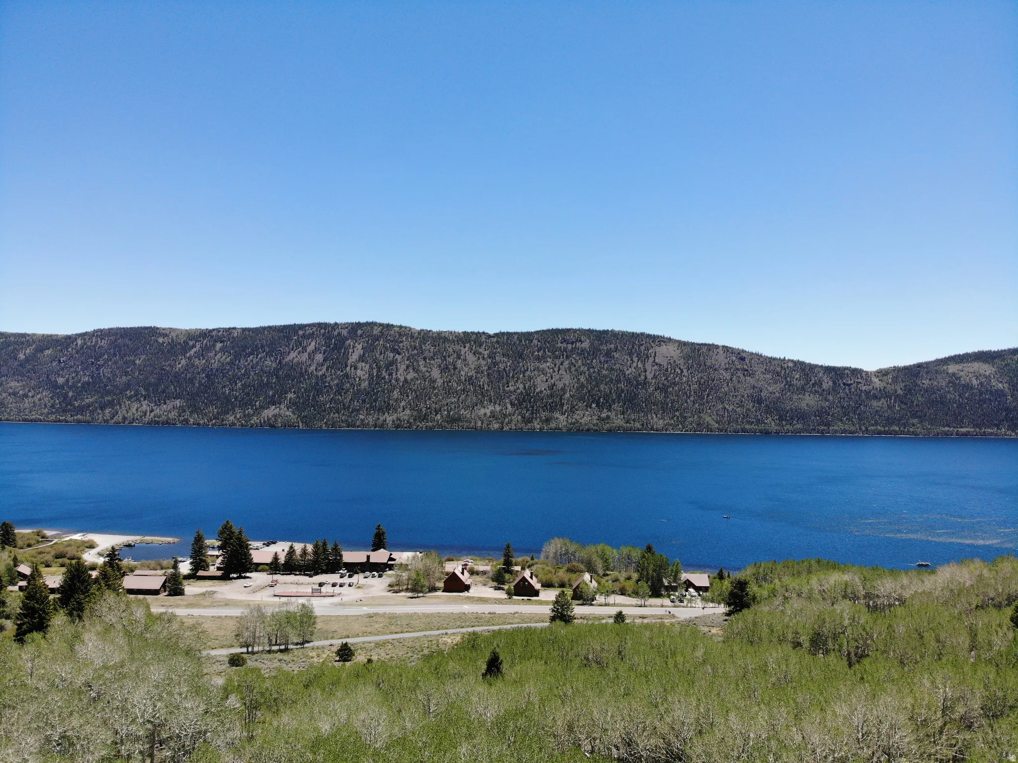 Expansive lakefront setting featuring several structures, a sandy shoreline, and mature trees