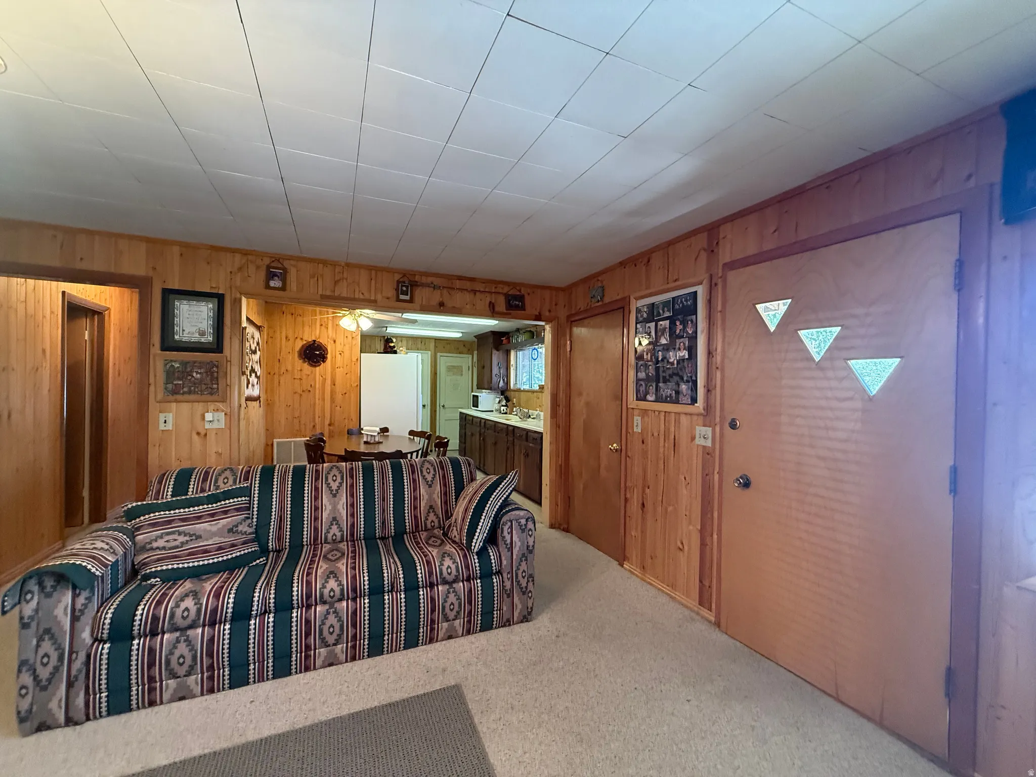 Wood-paneled living area with light-colored carpeting, featuring a doorway opening to an additional space and a wood door with decorative glass accents