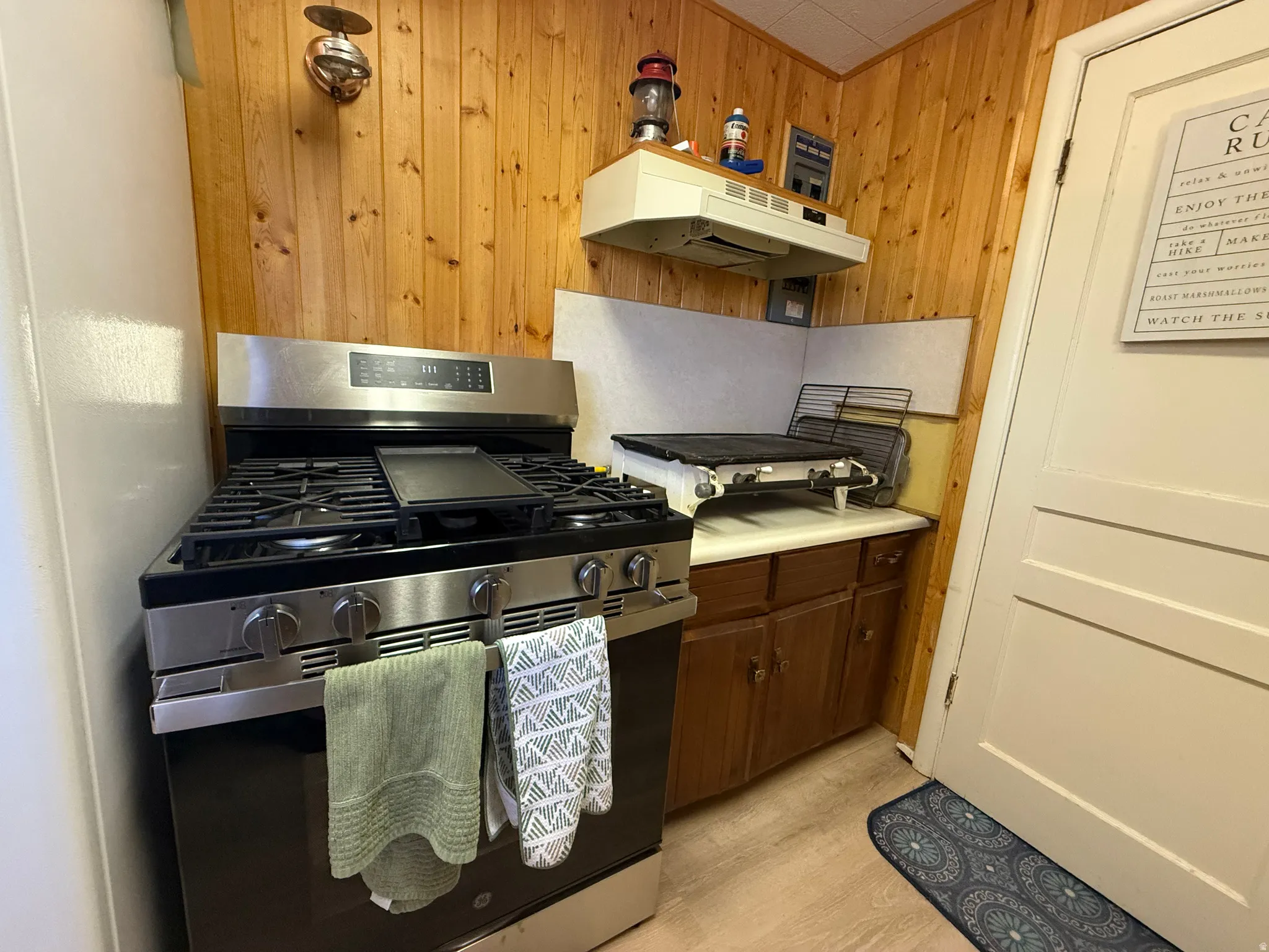 Stainless steel range with a built-in griddle, wood-finish wall paneling, white laminate countertops, and dark wood cabinetry