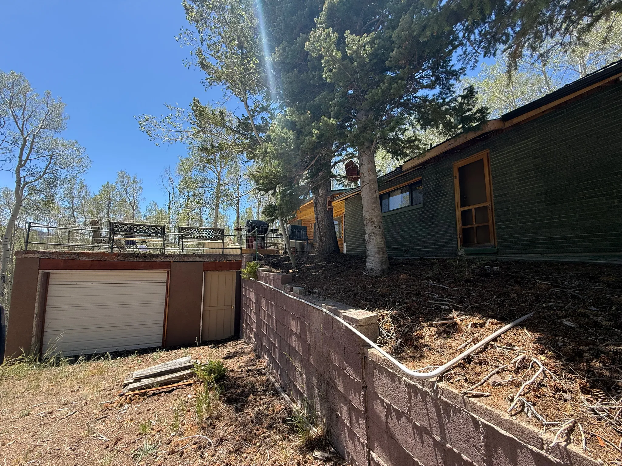 Lower-level attached garage with a roll-up door, complemented by an exterior retaining wall and an upper-level patio featuring a metal railing