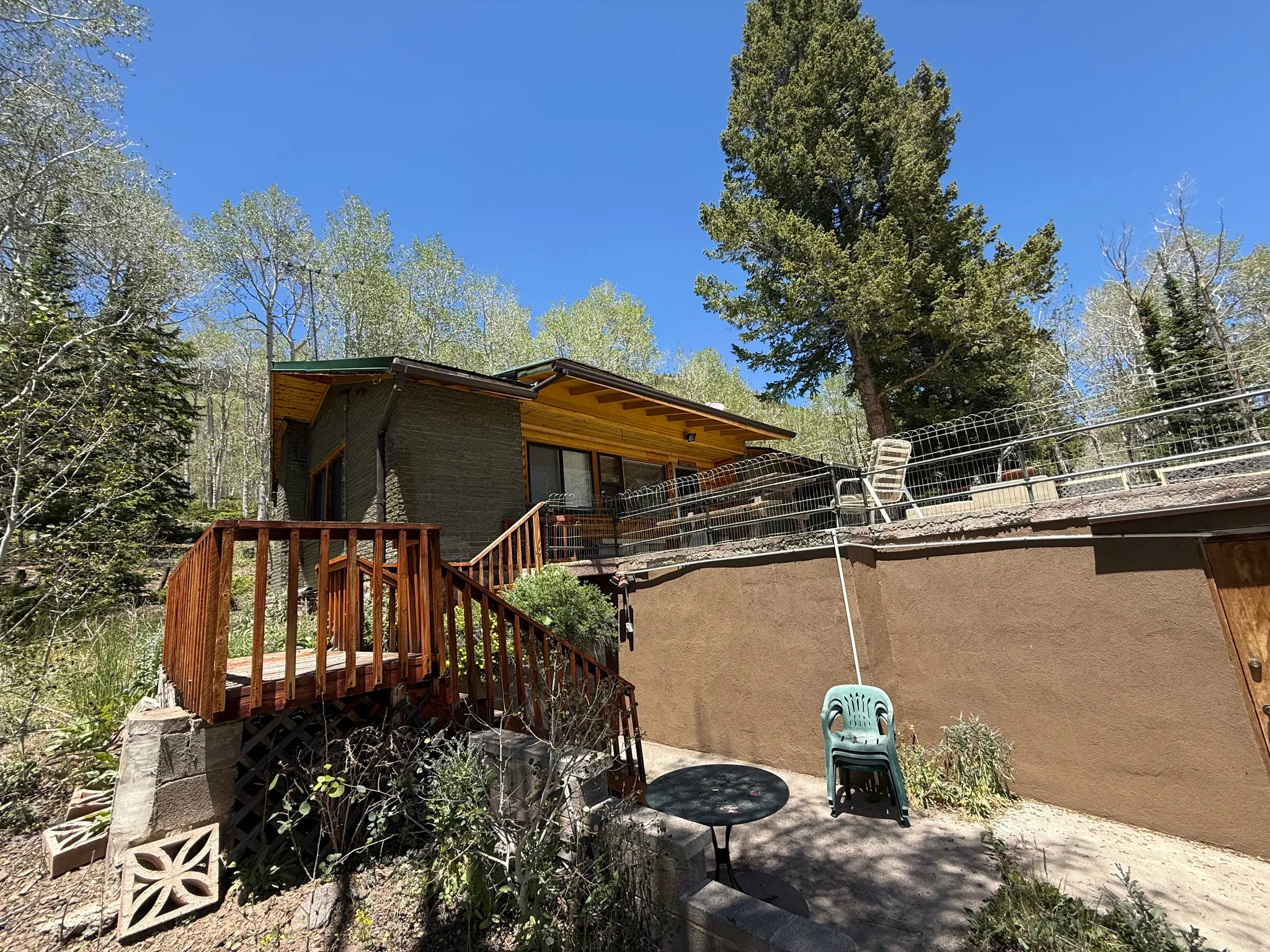 Split-level property featuring a wood-finish deck and stairs, stucco-finish lower level, and an upper-level patio with metal railing