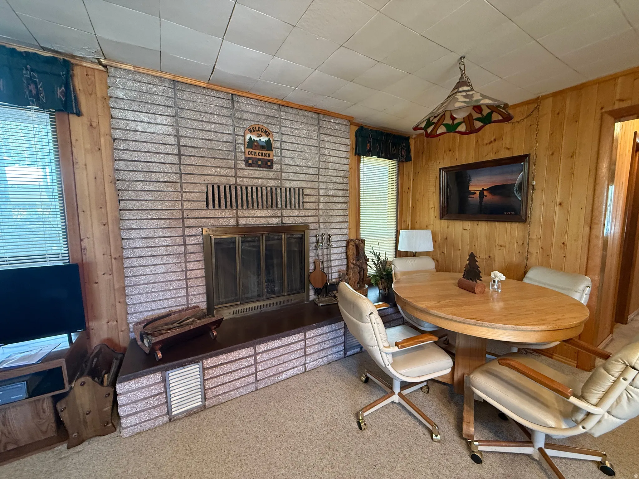 Interior space featuring a brick fireplace with a metal insert, wood-paneled walls, and a tiled ceiling