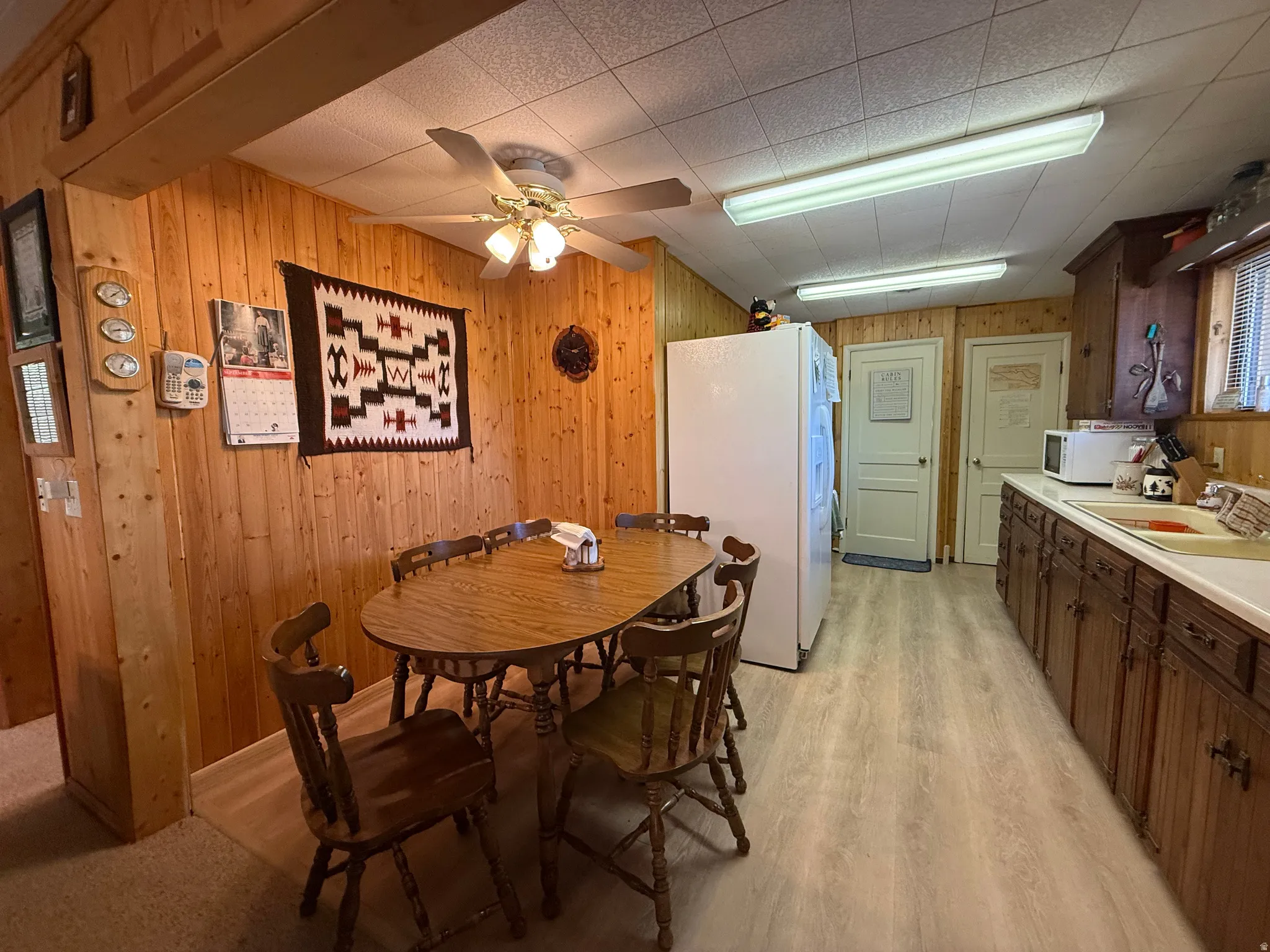 Spacious kitchen and dining area featuring wood-paneled walls, wood-finish flooring, and a ceiling fan with integrated lighting