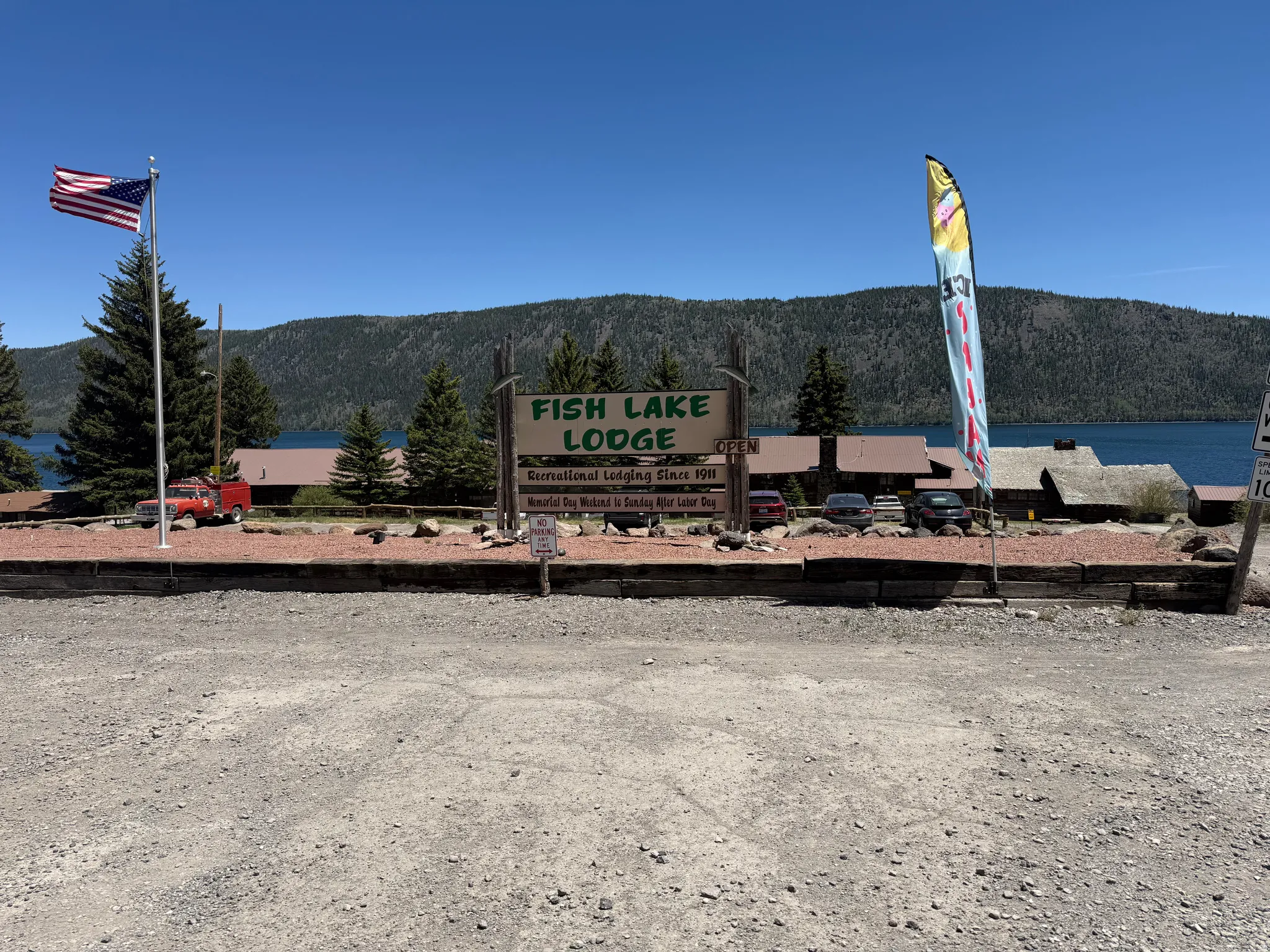Lakeside property featuring multiple structures, a prominent lodge sign, and a large gravel parking area