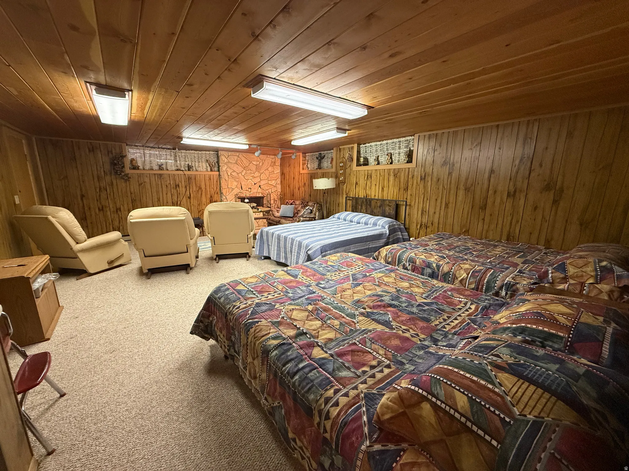 Wood-paneled room featuring a stone-faced fireplace, recessed shelf display, planked wood ceiling, and carpeted flooring