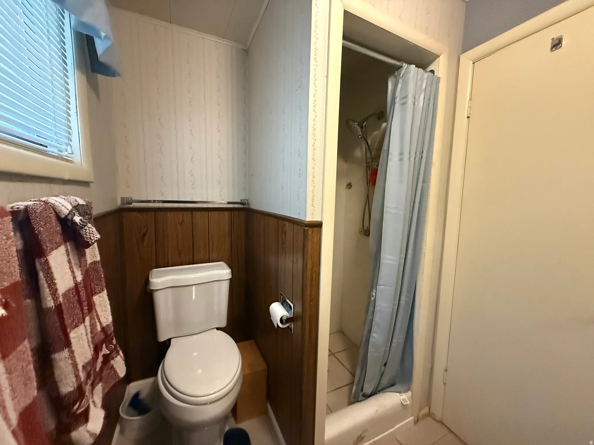 Bathroom featuring a standard toilet, wood paneling, and a separate shower stall with tile flooring