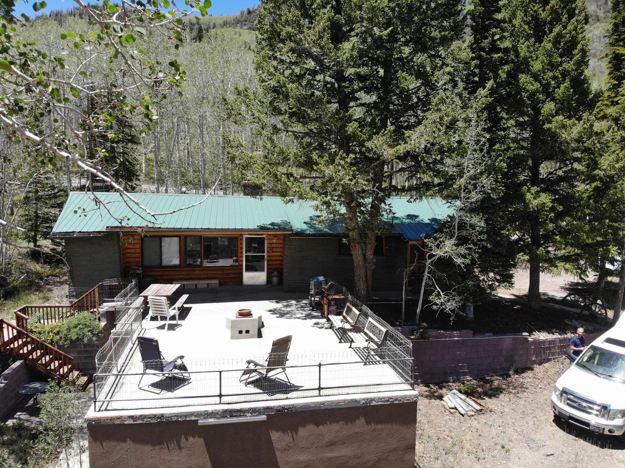Log cabin exterior with a green metal roof, featuring an expansive concrete patio with a metal railing
