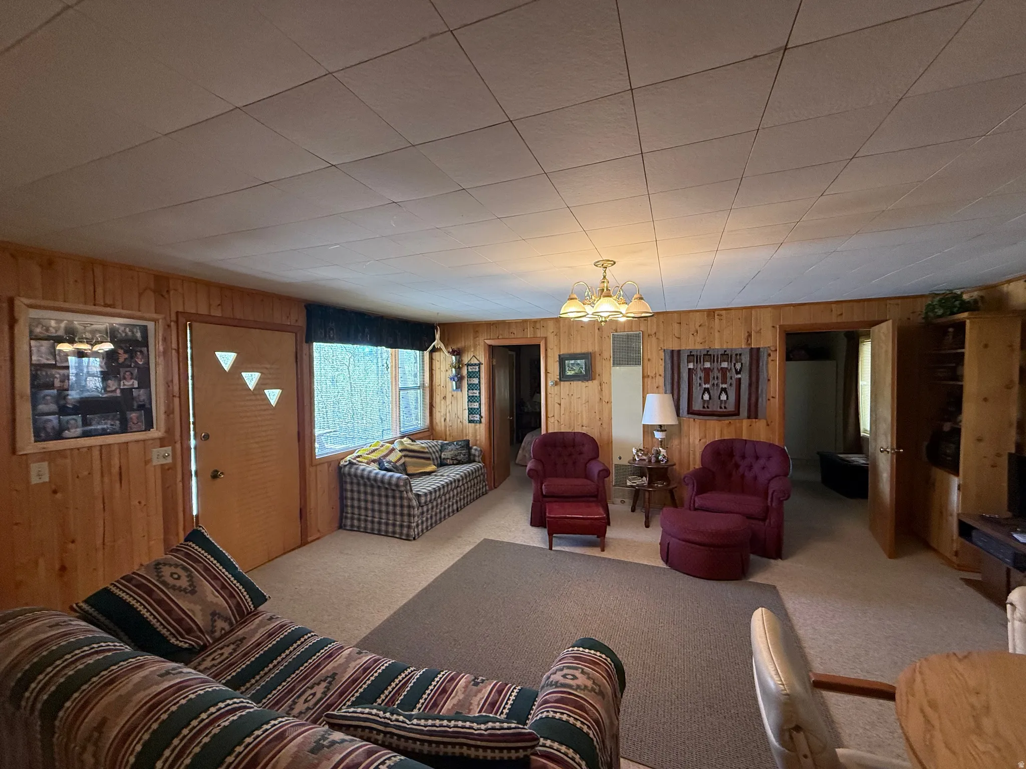 Living room with natural wood-paneled walls, a drop ceiling, and carpet flooring