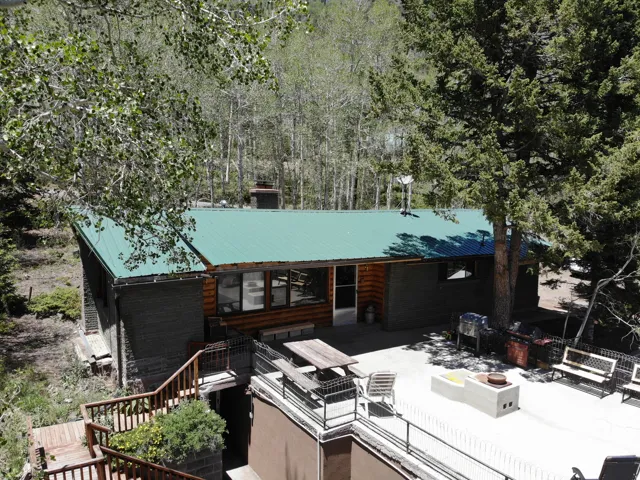 Log cabin exterior with a green metal roof, featuring a large concrete patio, a built-in outdoor fire pit, and a multi-level wooden deck with railing