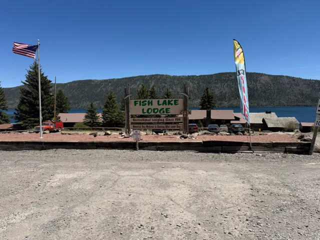 Lakeside property featuring multiple structures, a prominent lodge sign, and a large gravel parking area