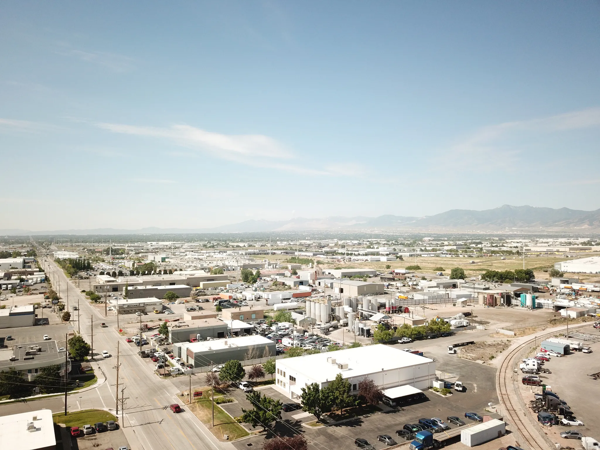 Aerial perspective of an industrial landscape featuring multiple commercial buildings, paved roadways, and a clear mountain range backdrop