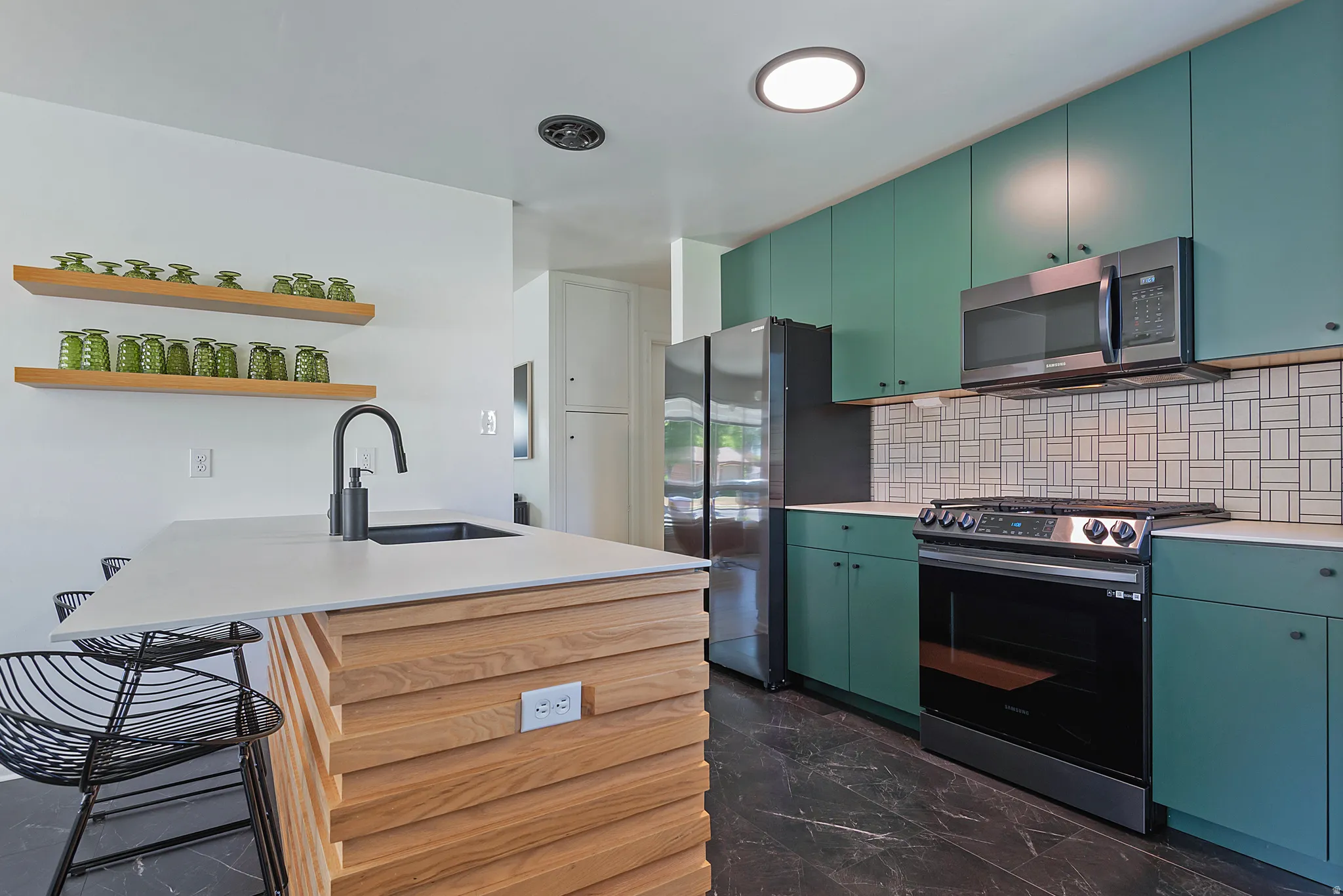 Kitchen featuring an integrated island with a black sink and faucet, green cabinetry, white countertops, and a tiled backsplash