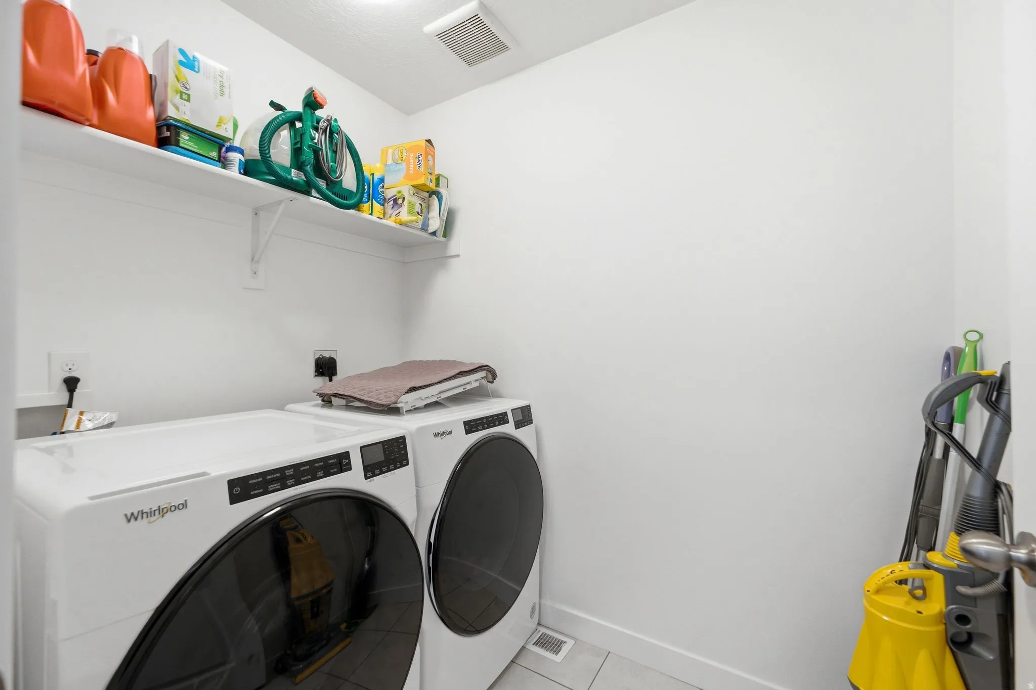 Dedicated laundry area featuring a white floating shelf, white walls, and light-toned flooring