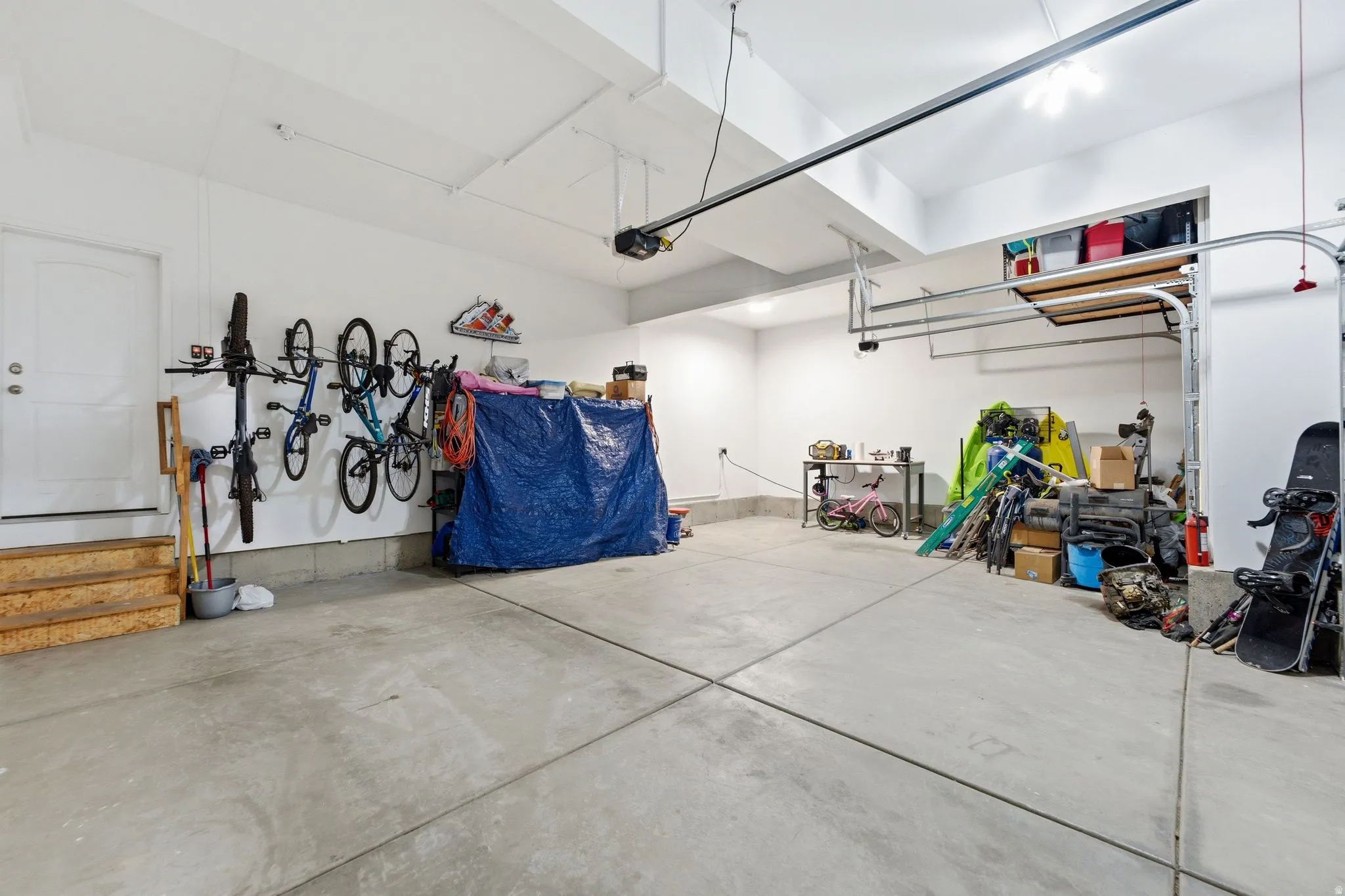 Spacious 3- car garage with concrete flooring, white painted walls, and overhead lighting & storage