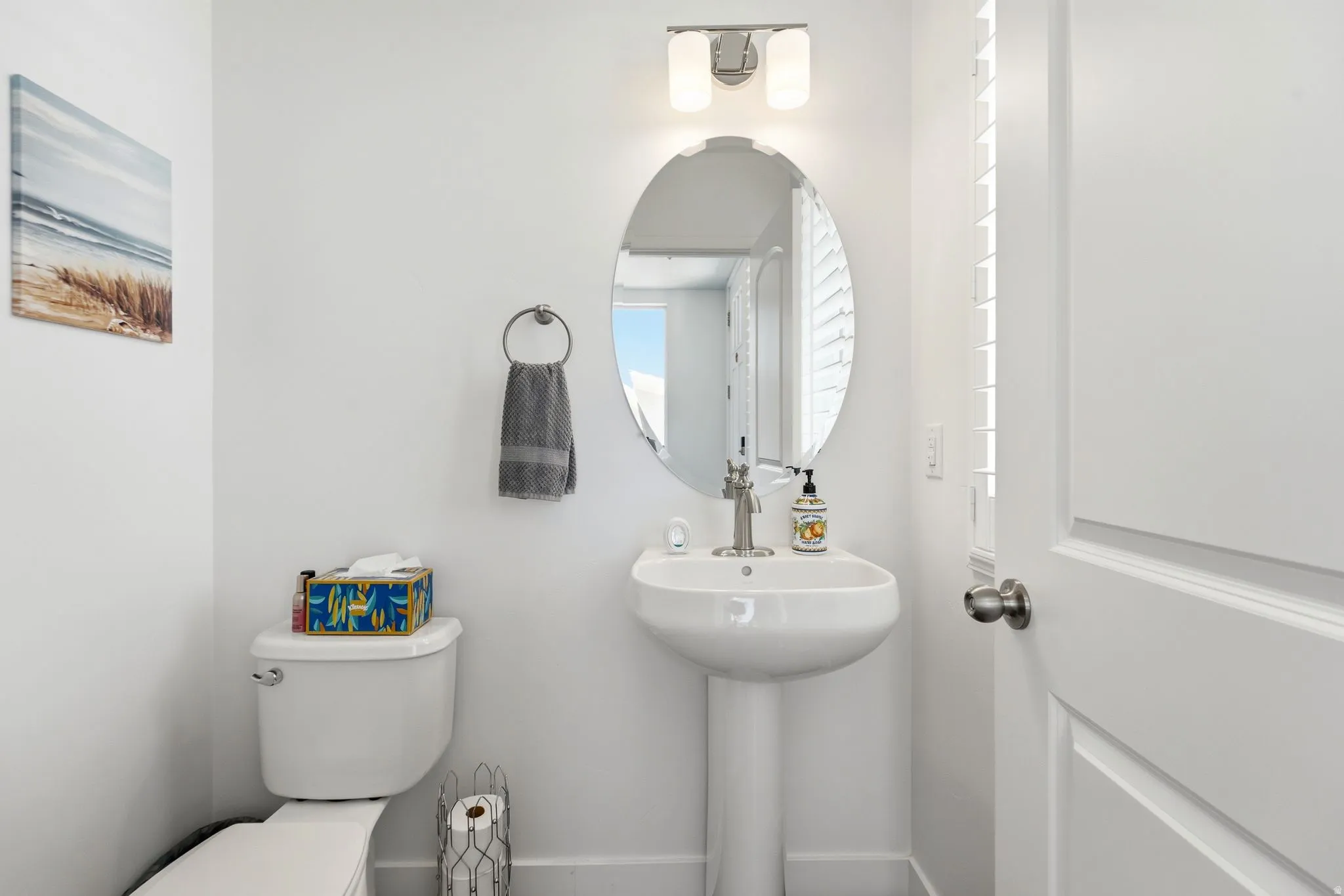 Pedestal sink with a brushed nickel faucet and oval mirror