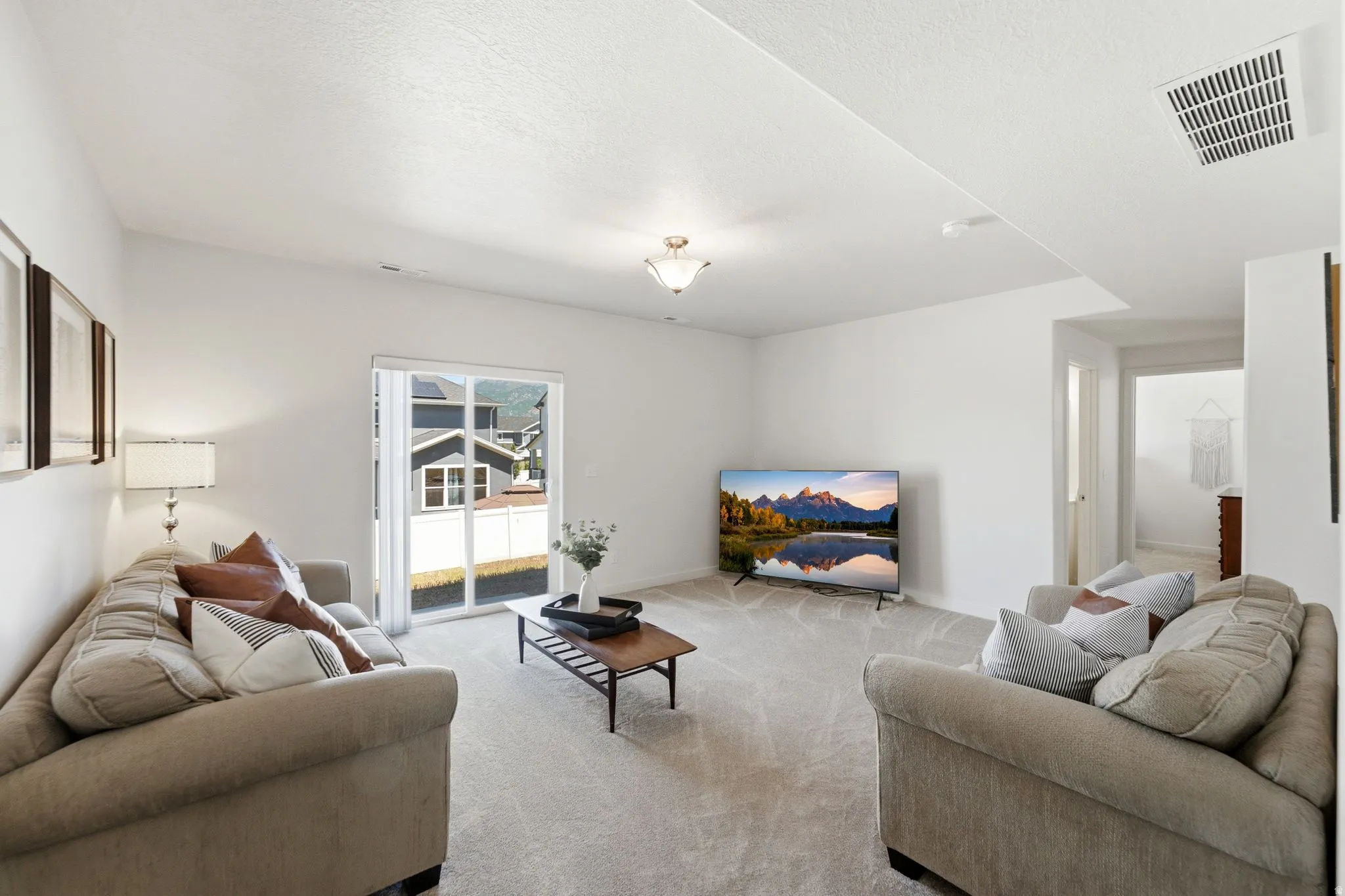 Carpeted living area featuring white walls, a ceiling-mounted light fixture, and sliding glass doors providing access to the exterior