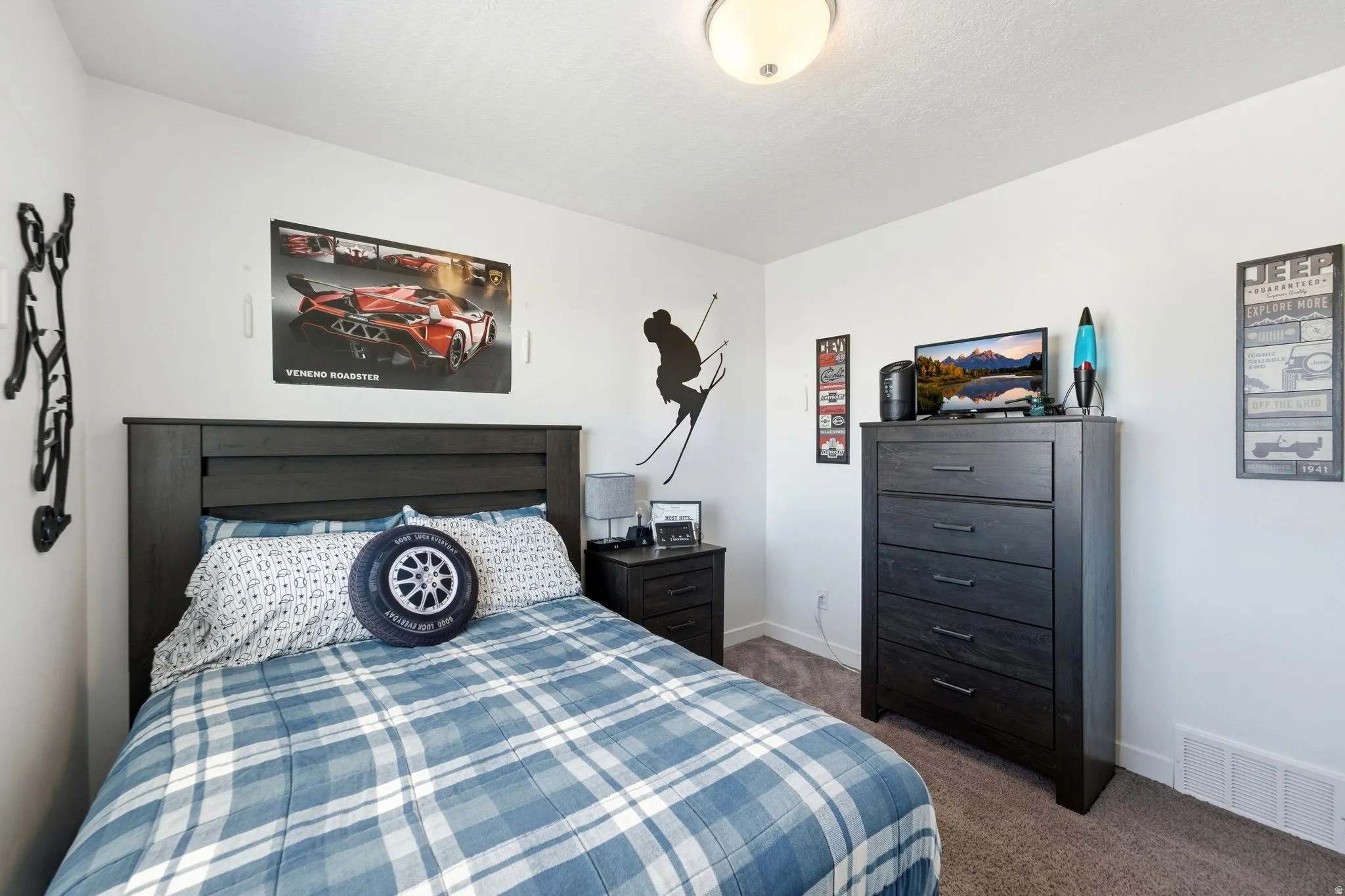 Spacious bedroom featuring neutral wall tones, textured carpet flooring, and a contemporary ceiling light fixture