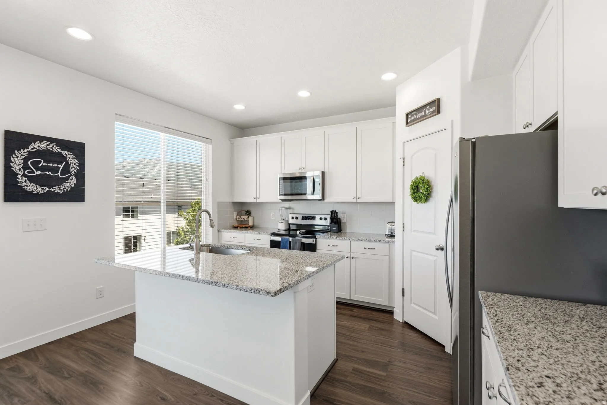 Modern kitchen featuring white cabinetry, granite countertops, stainless steel appliances, wood-finish flooring, and recessed lighting