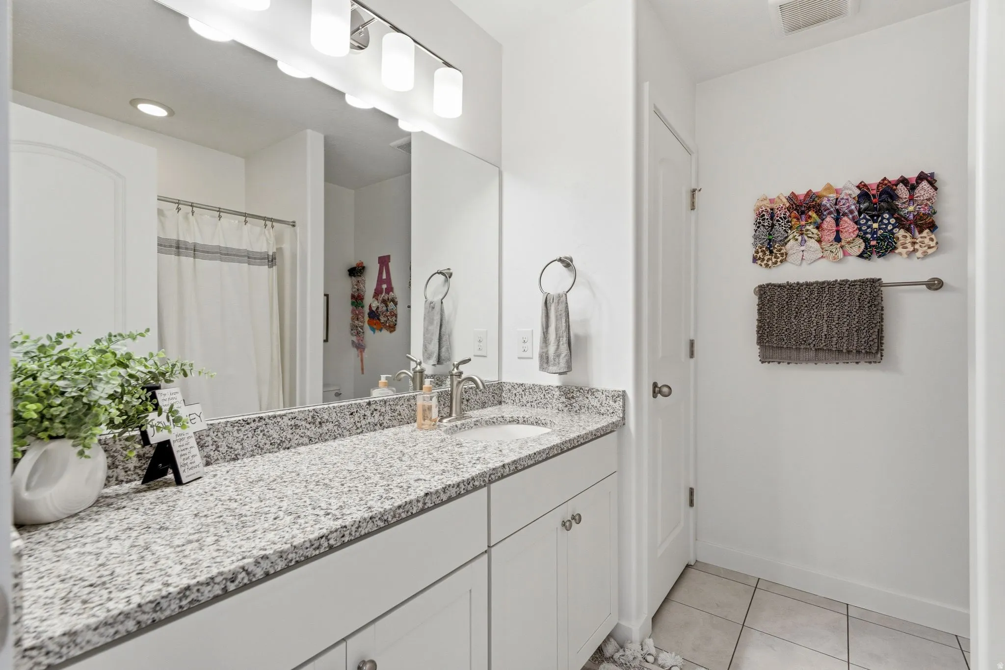 Bathroom featuring a double vanity with stone-finish countertops, white cabinetry, a single basin sink, and tile flooring
