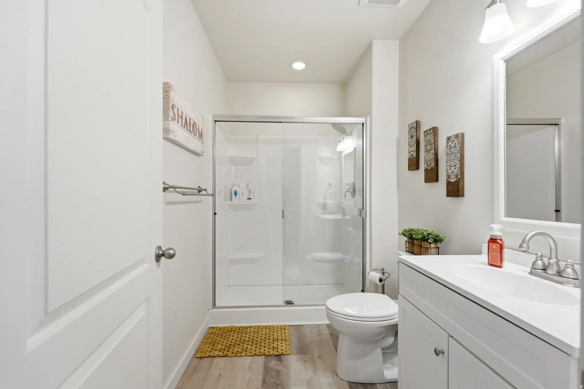 Bathroom featuring a glass-enclosed shower, single vanity with a white countertop, recessed lighting, and wood-finish flooring