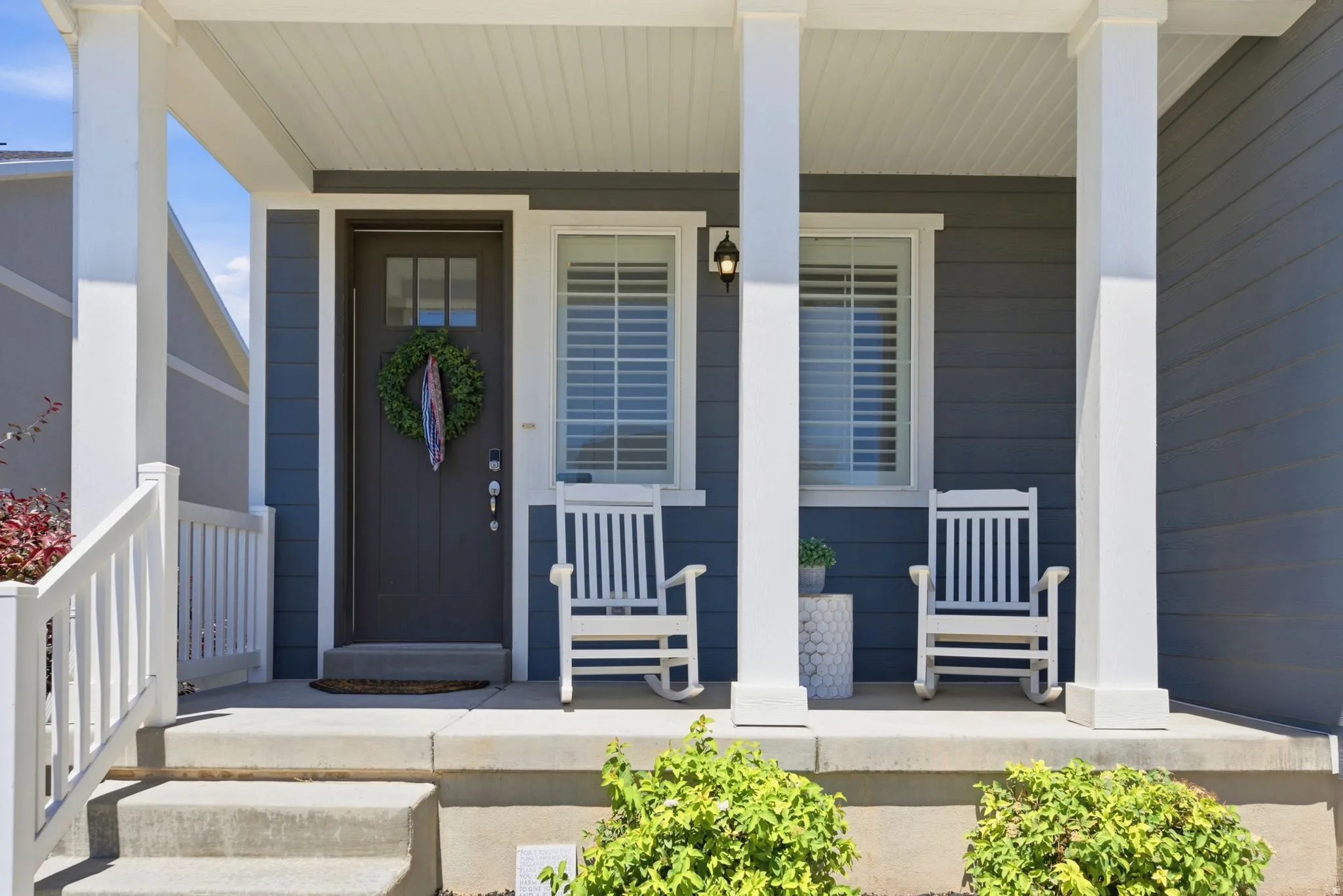 Inviting front porch featuring a dark entry door with upper glass panels, a white railing, and substantial white pillars