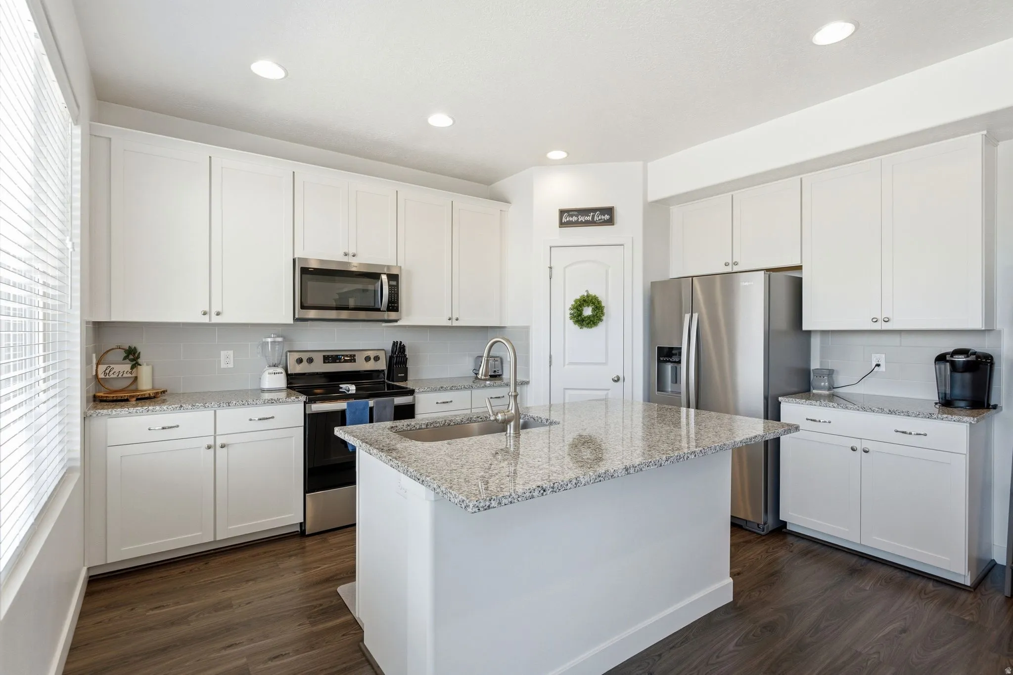 Kitchen featuring a central island with an undermount sink, granite countertops, white cabinetry, and wood-finish flooring
