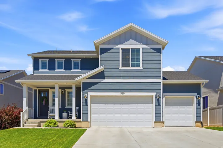 Two-story residence featuring blue siding, white trim, a covered front porch with white pillars, a two-car garage, and a single-car garage