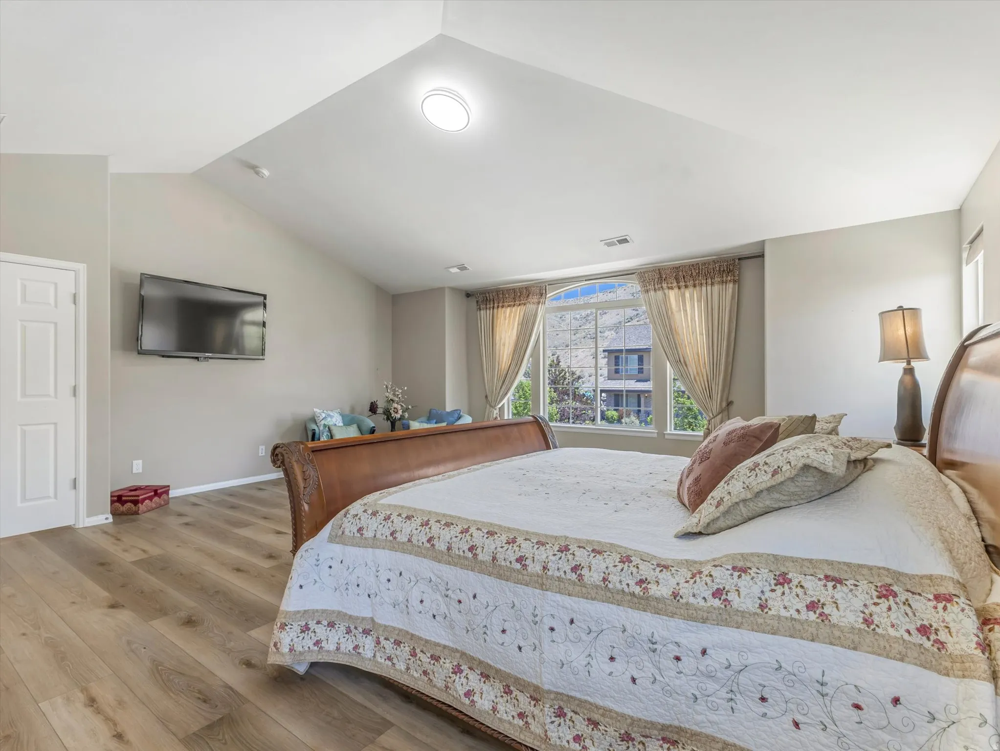 Spacious room featuring vaulted ceilings, wood-finish flooring, and a large bay window