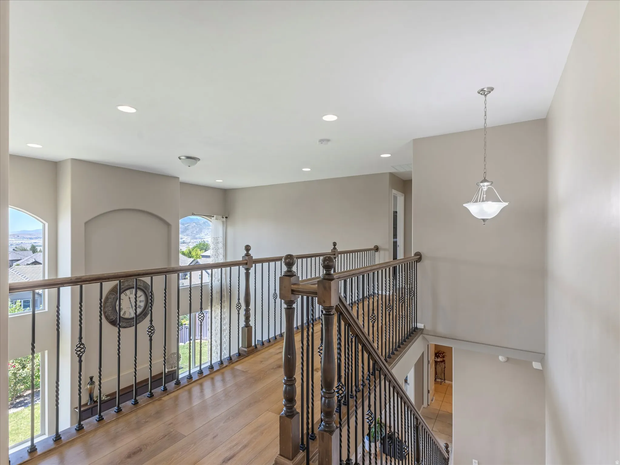 Upper-level hallway featuring wood-finish flooring, wrought iron balusters, recessed lighting, and arched windows providing natural illumination