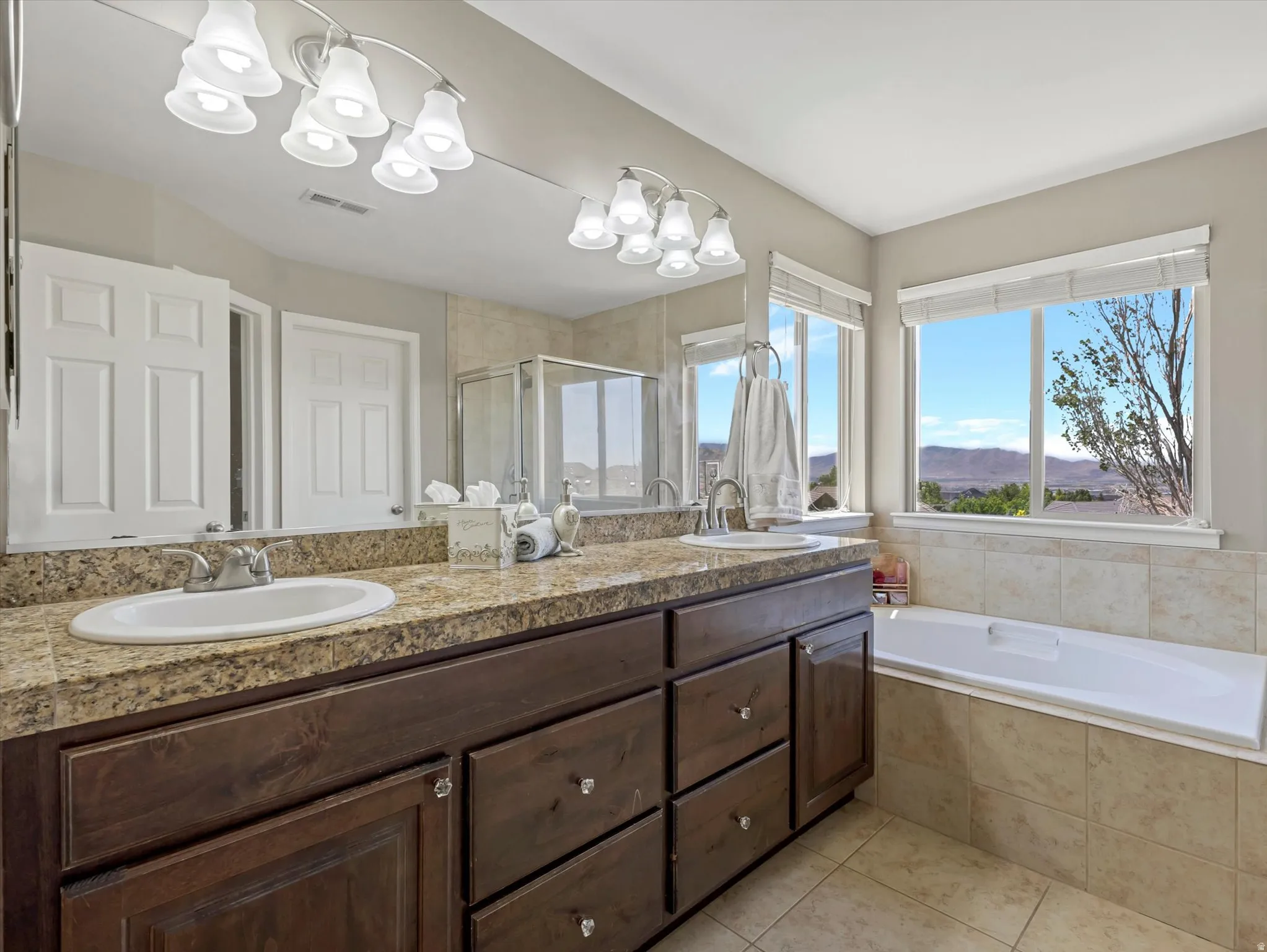 Bathroom featuring a double vanity with stone-finish countertop, dark wood cabinetry, dual sinks, and an integrated bathtub