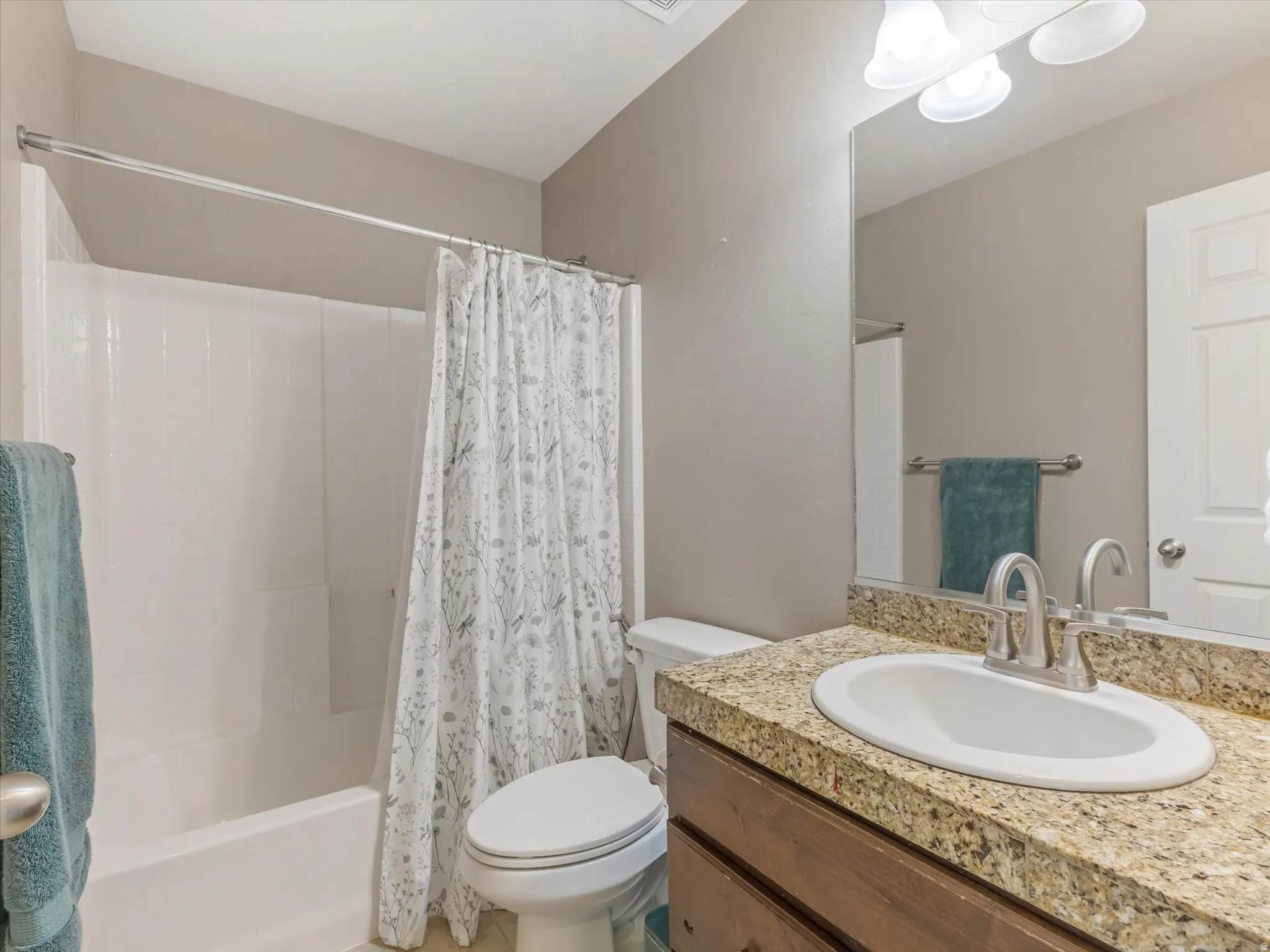 Bathroom featuring a white tub/shower combination, a vanity with a granite countertop, an undermount sink, and a brushed nickel faucet
