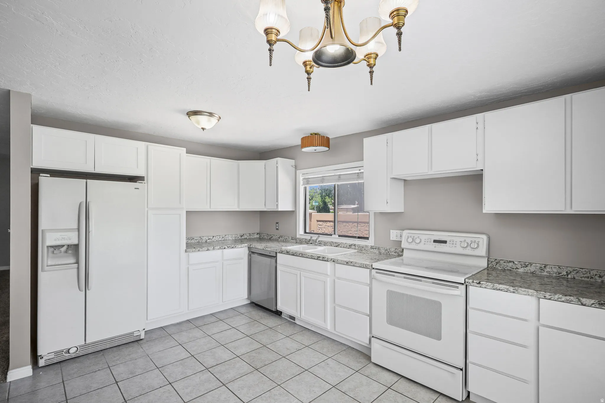 Kitchen featuring white cabinetry, gray tile flooring, stone-look countertops, and white appliances