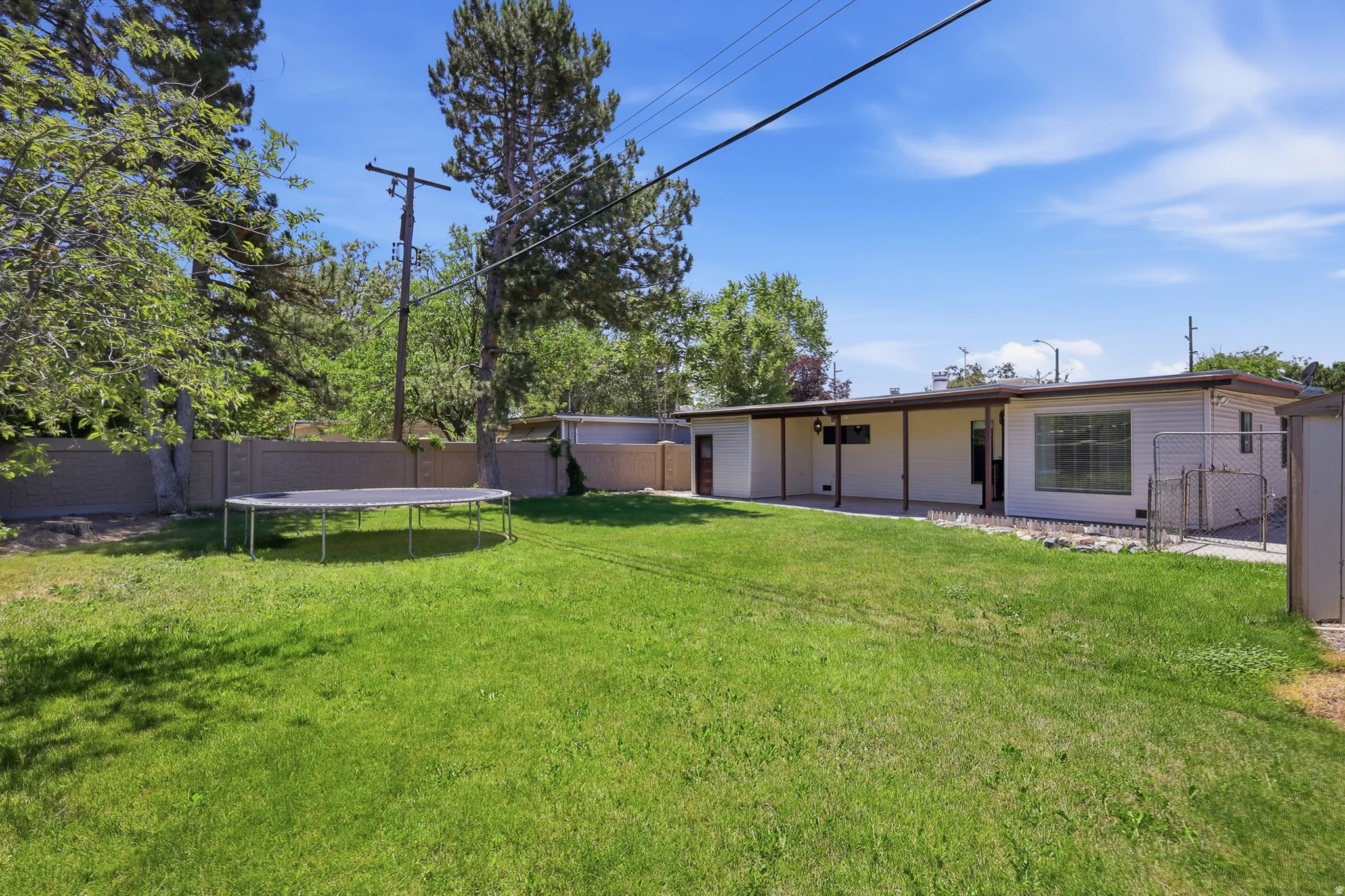 Expansive backyard featuring a manicured lawn, partial privacy fencing, and mature trees