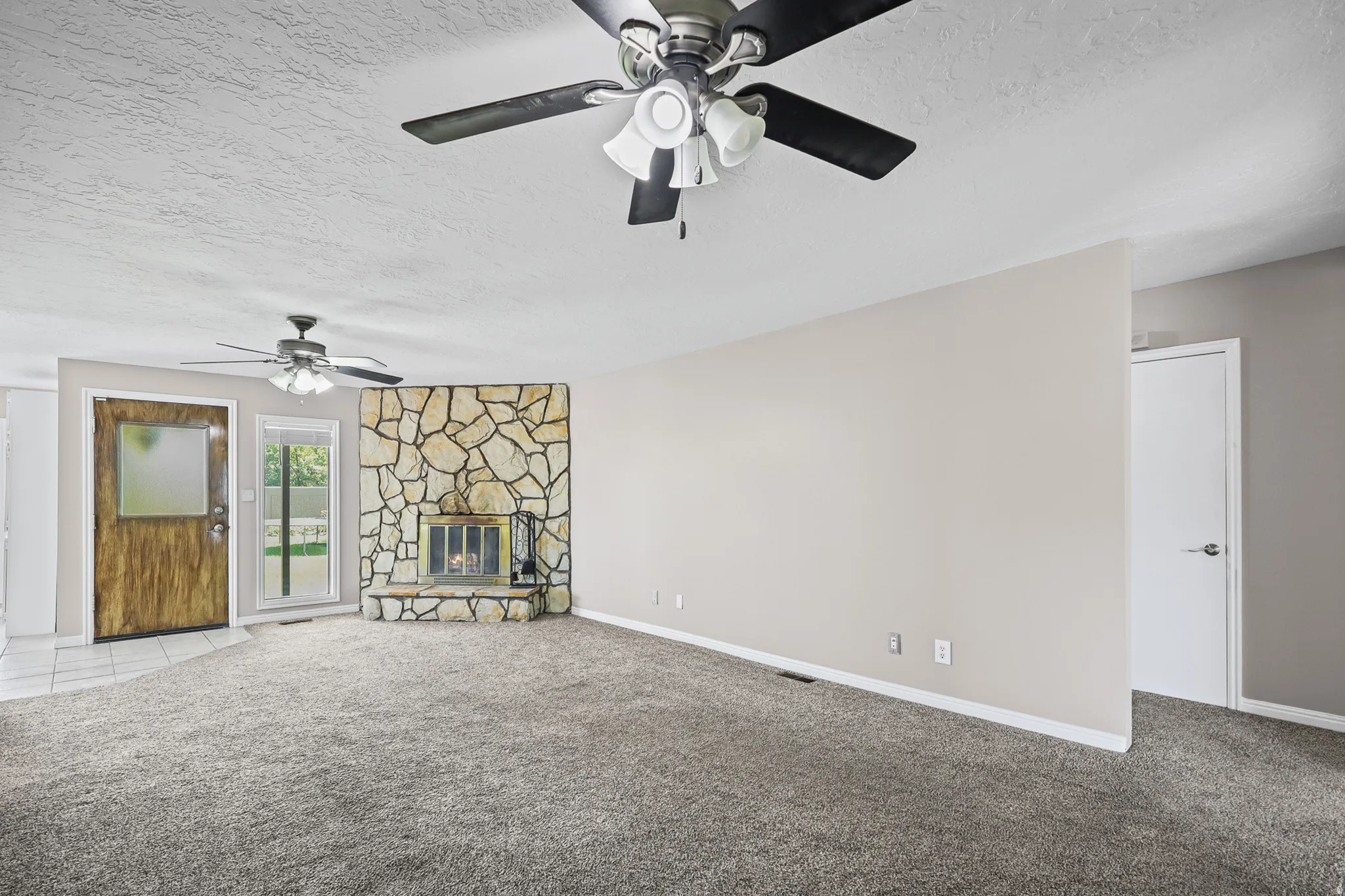 Spacious living area featuring a floor-to-ceiling stone fireplace surround, glass patio door, and wood-finish entry door with frosted glass panel
