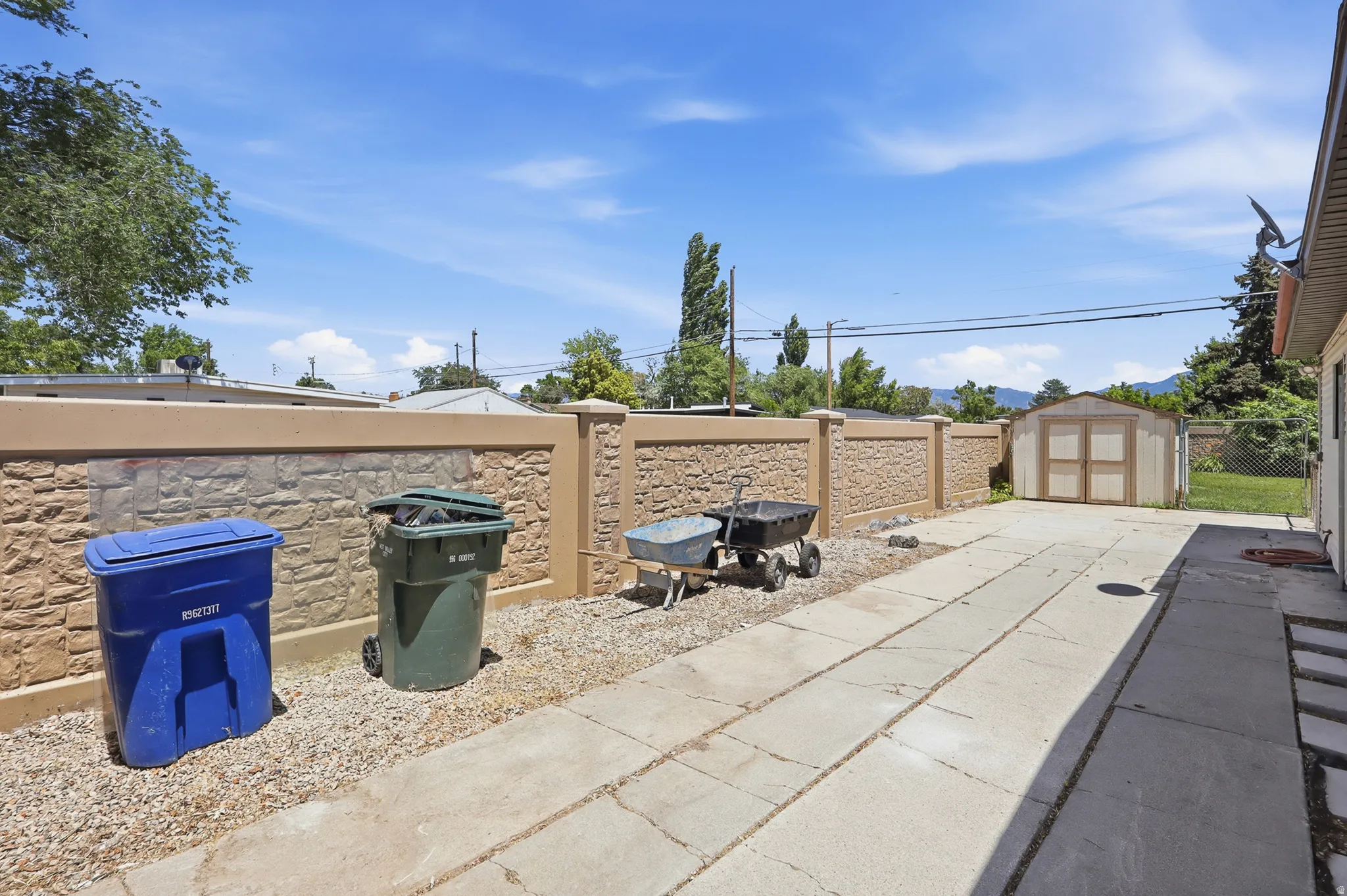 Concrete patio space featuring a stone-look perimeter wall and a detached storage shed
