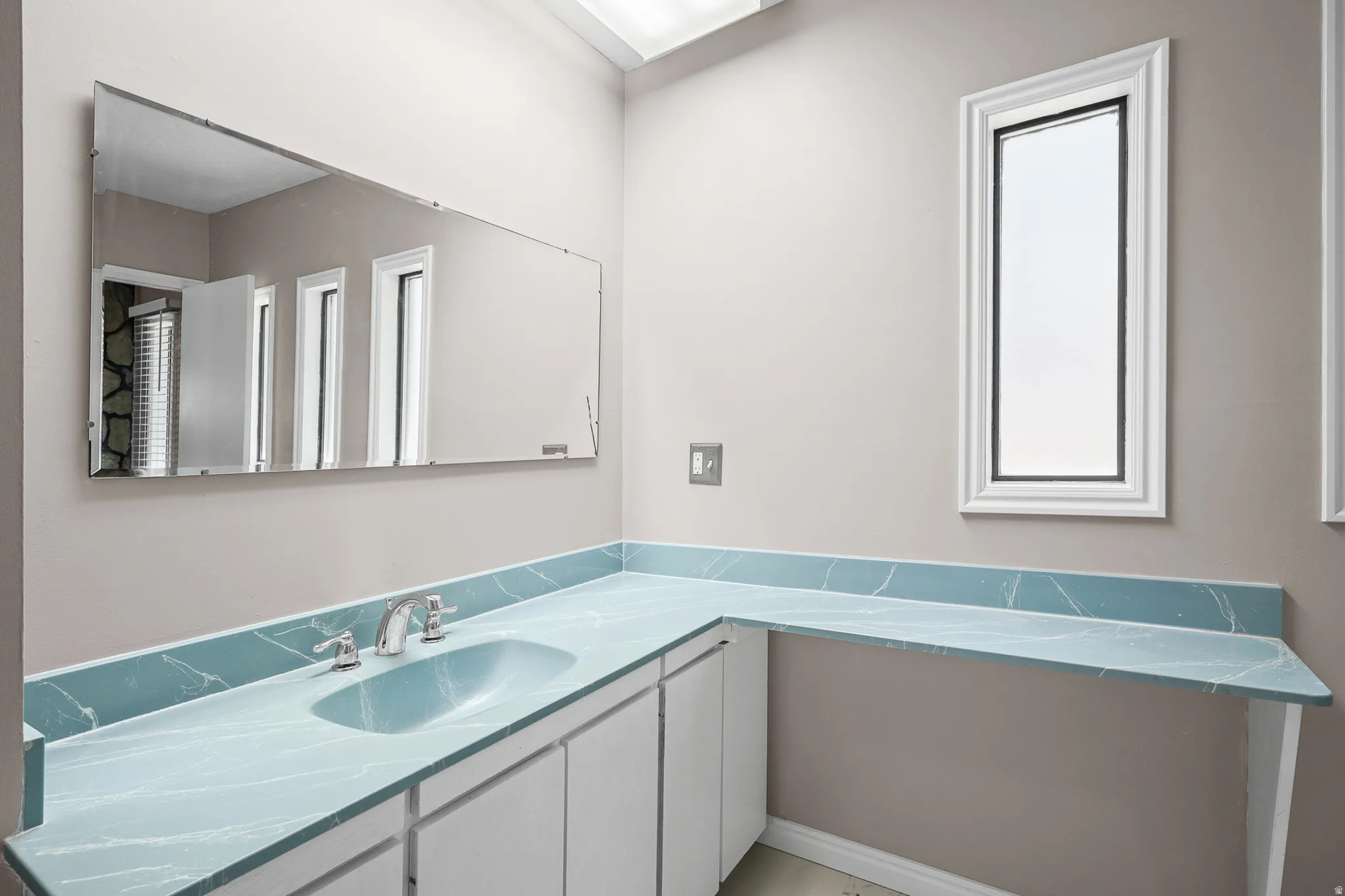 Bathroom vanity featuring a light blue countertop with white veining, an integrated oval sink, and chrome fixtures