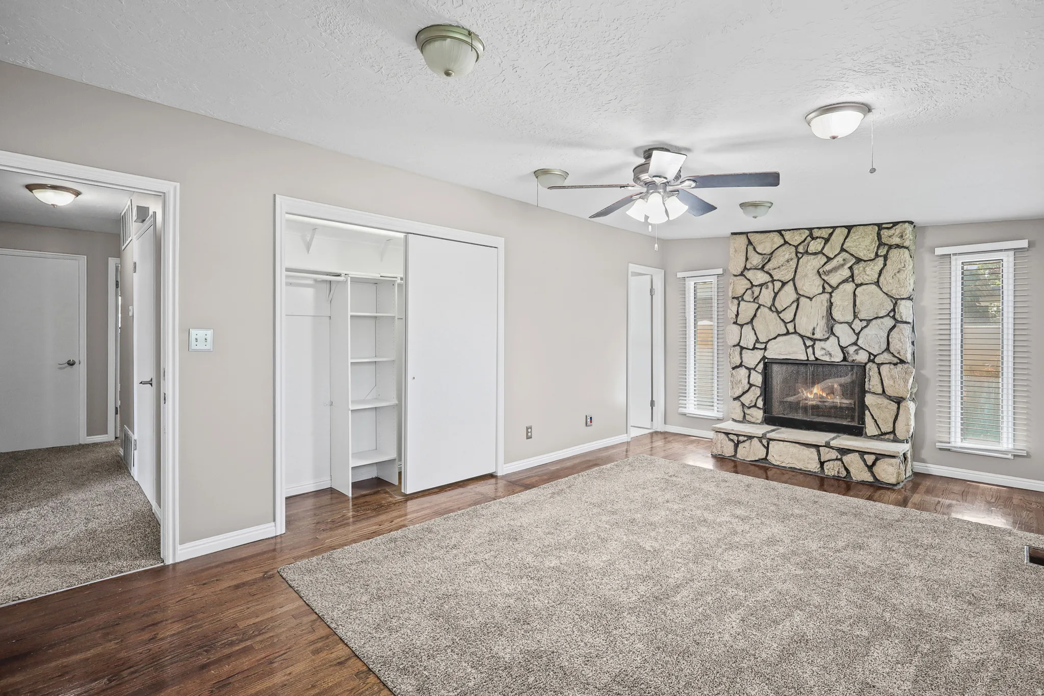 Spacious interior featuring a stone-clad fireplace, wood-finish flooring, and a ceiling fan