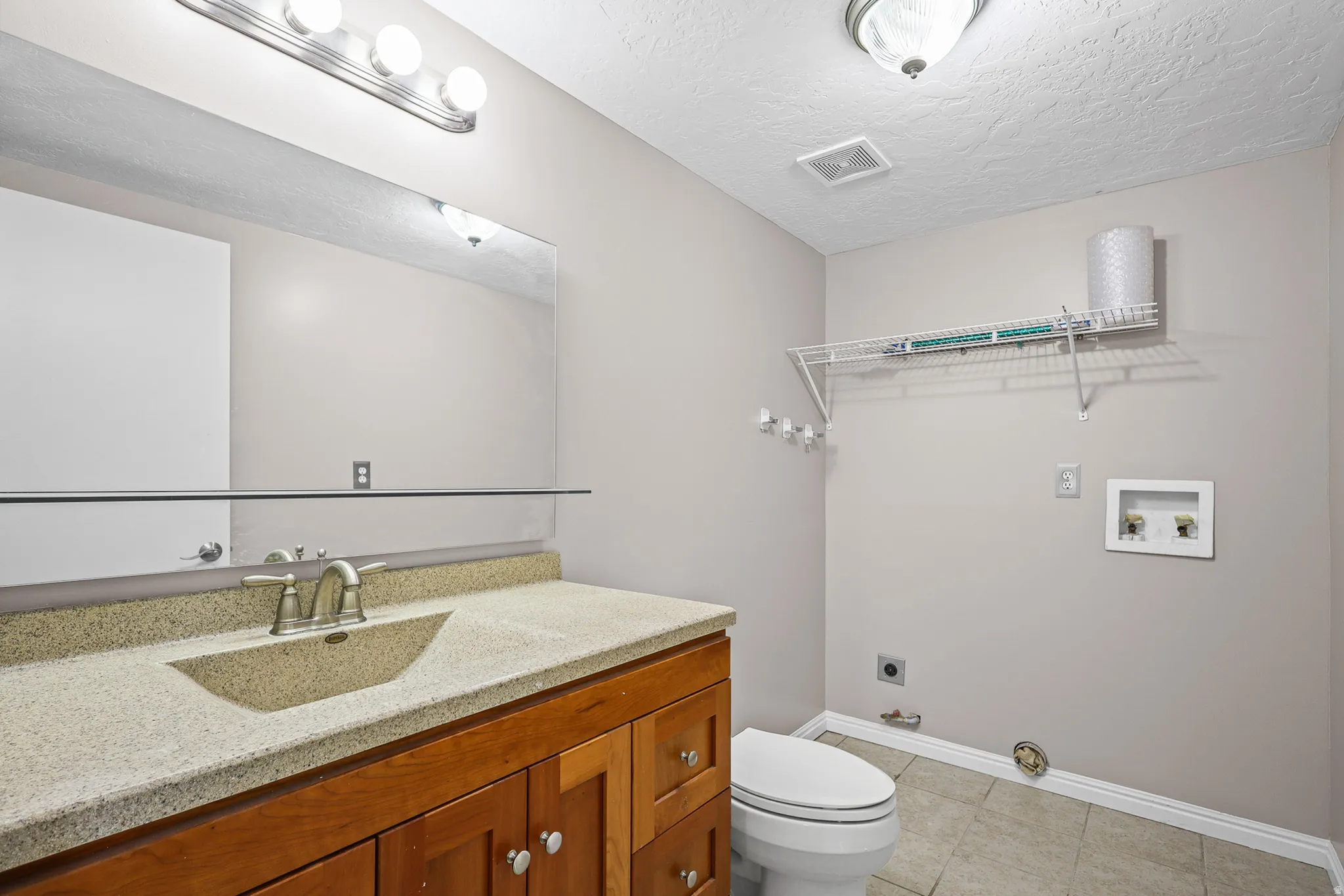 Vanity with an integrated sink and light-toned countertop, wood-finish cabinetry, and a full-width mirror