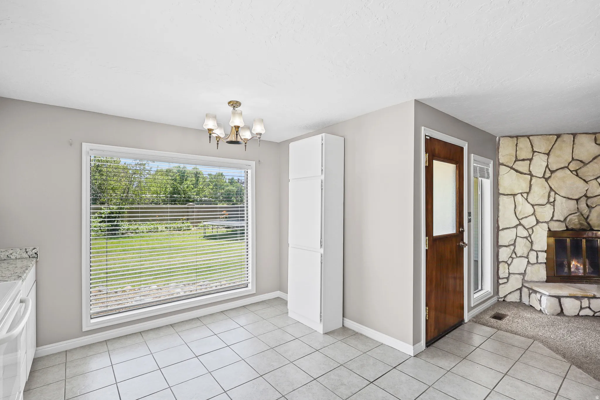 Dining area with large window overlooking green space, tile flooring, and a brass chandelier