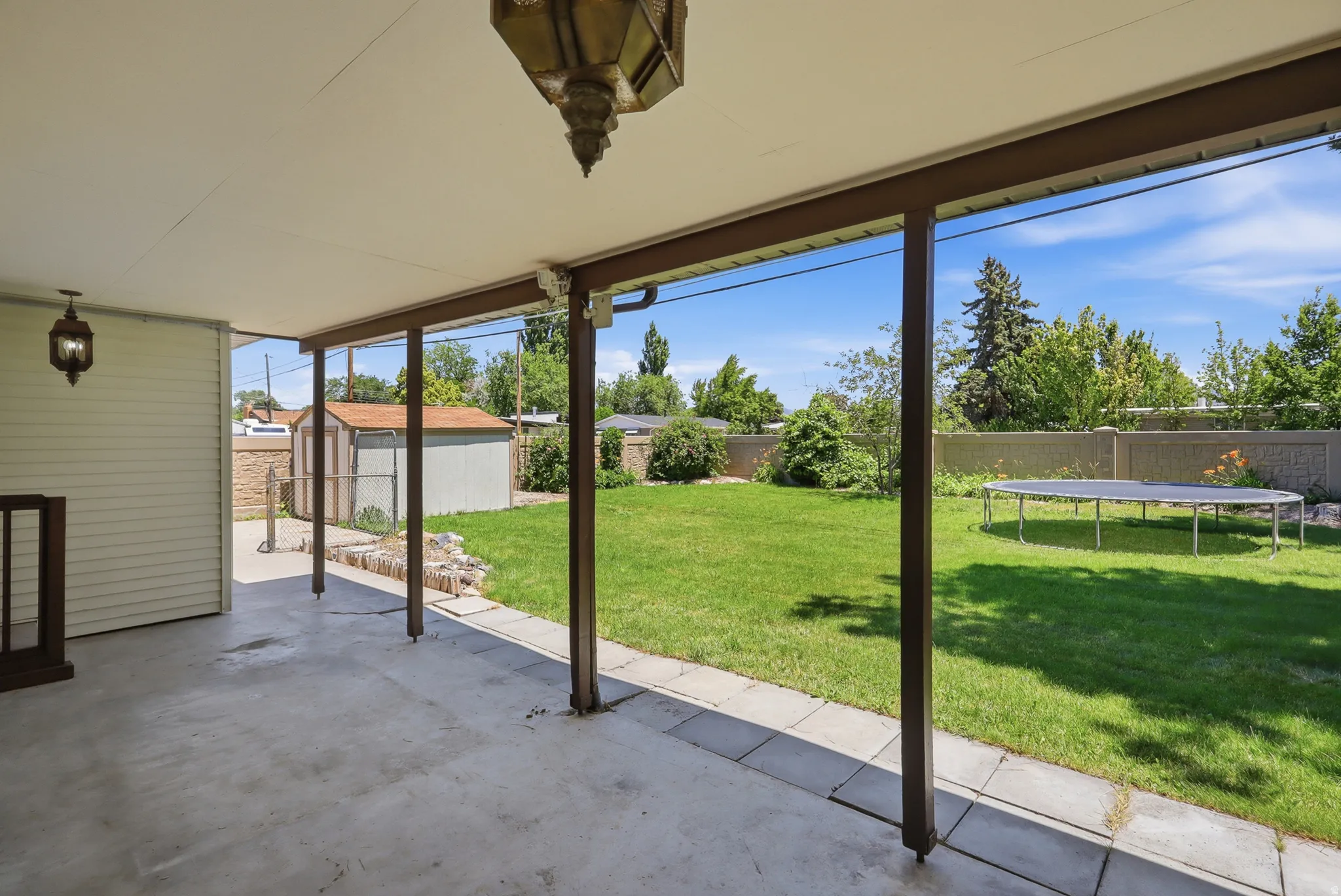 Covered patio with concrete flooring, supported by dark-toned posts, extending to a spacious grassy yard