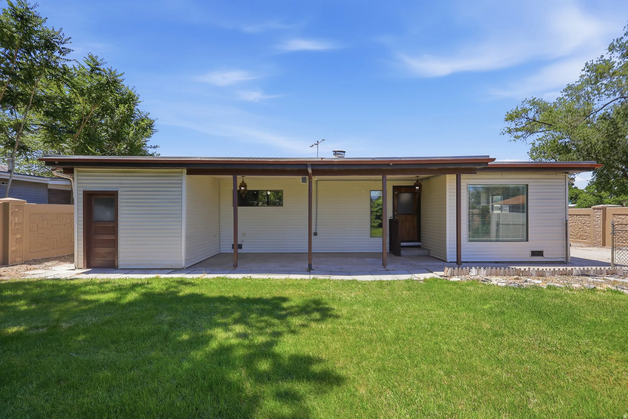 Rear exterior featuring a covered patio, neutral siding, a wood-paneled door, and a manicured lawn