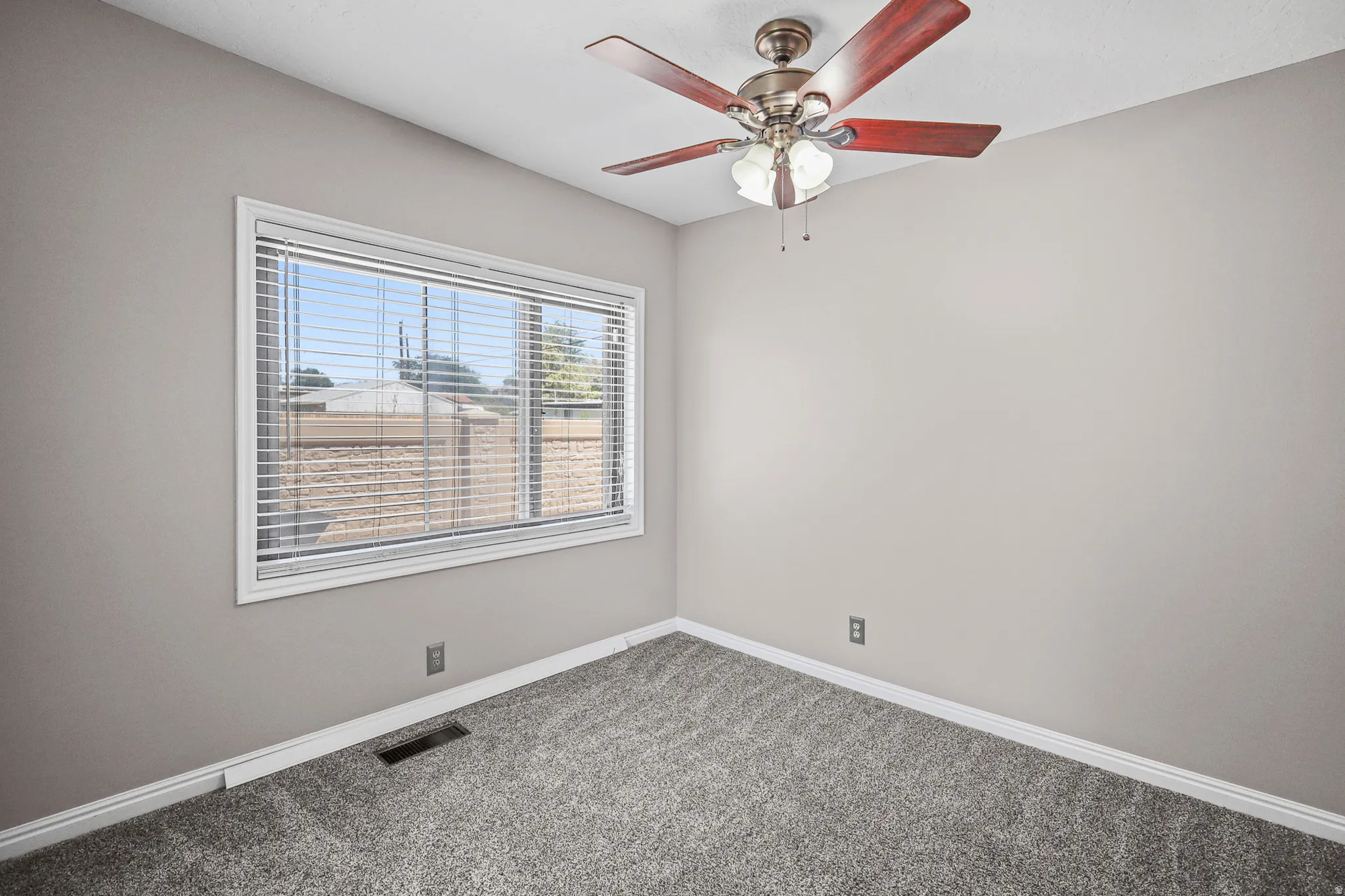 Carpeted room with a ceiling fan featuring wood-finish blades and an integrated light fixture