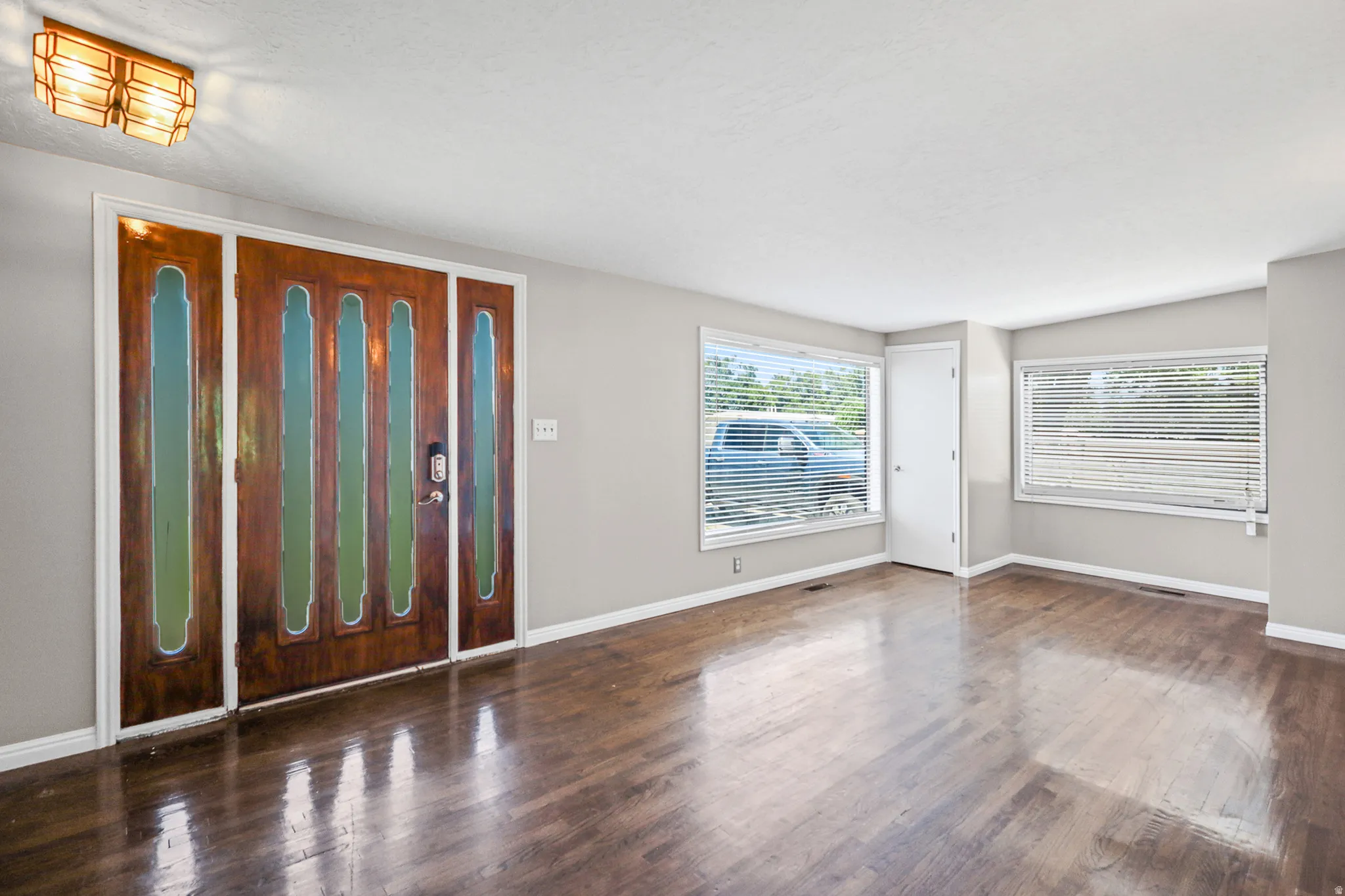 Entryway featuring a rich wood-finish door with decorative glass inserts, complemented by light gray painted walls and dark wood-finish flooring