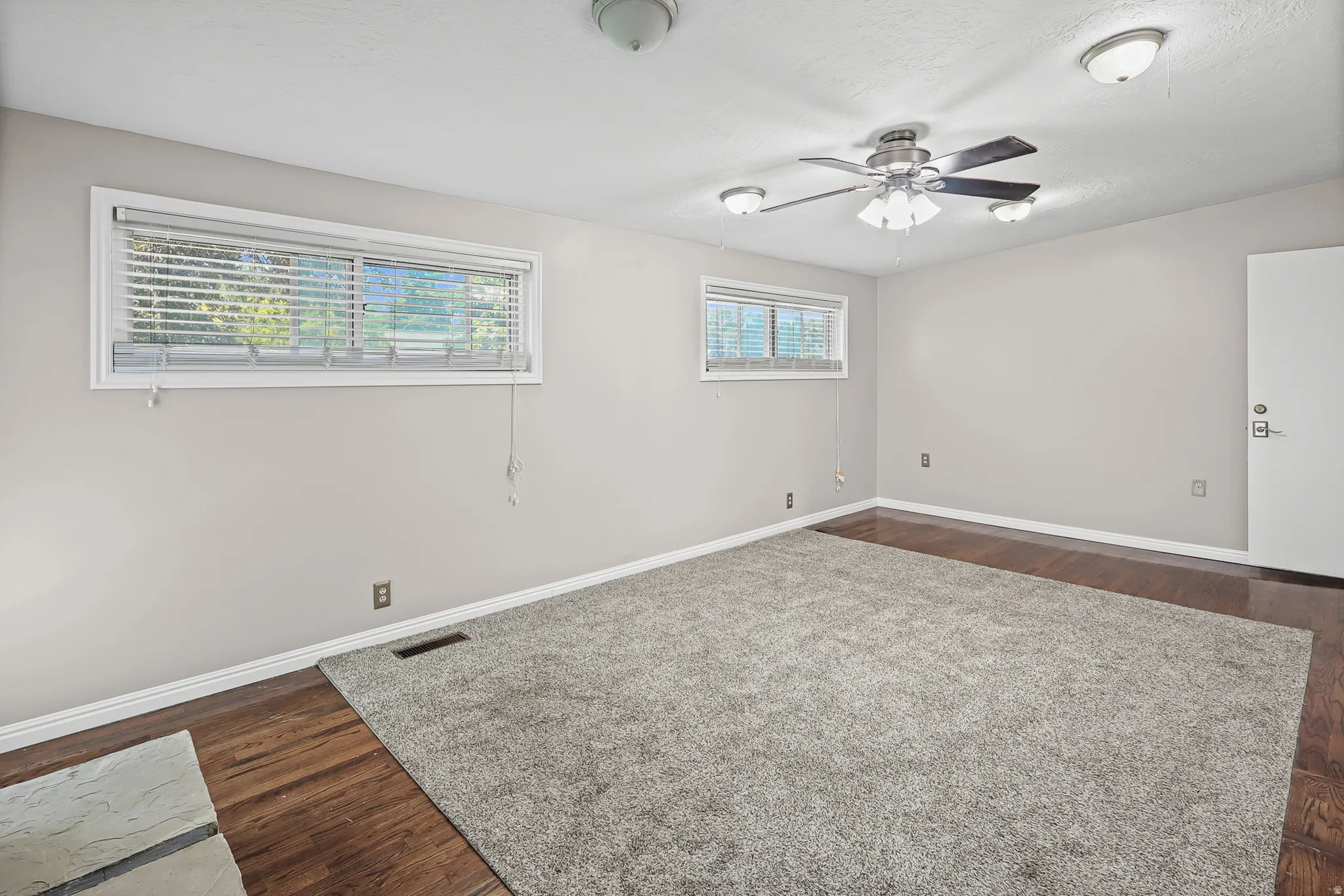 Spacious room featuring neutral painted walls and a combination of wood-finish flooring and plush carpeting