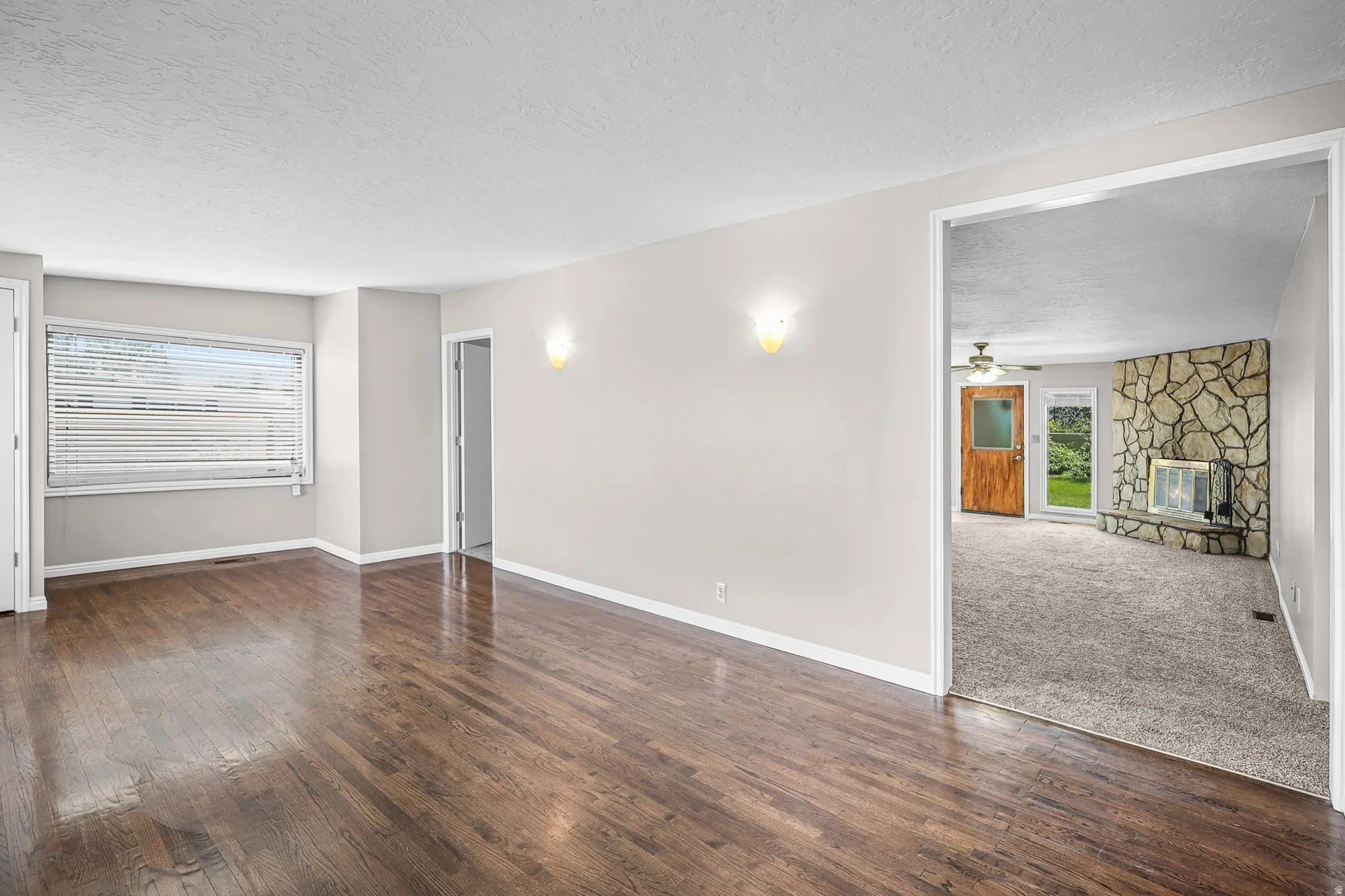 Spacious room featuring wood-finish flooring, light grey walls, and a large window with blinds